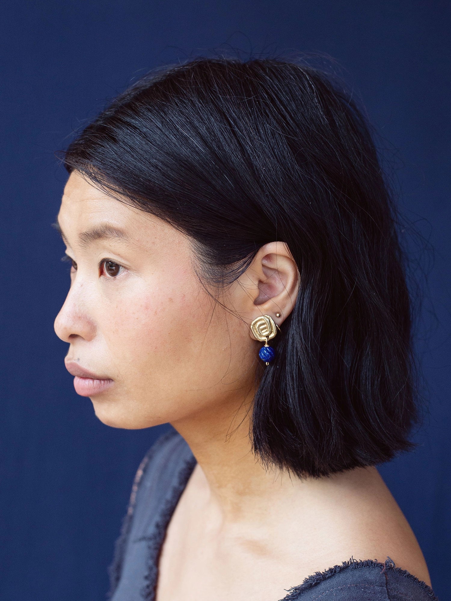 A woman wears a pair of hand-formed brass spiral drop earrings with lapis lazuli beaded stone by Canadian jewelry designer Michelle Ross