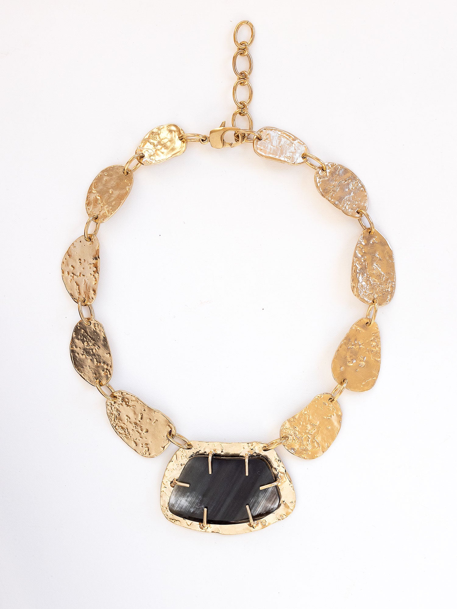 A brass statement necklace with hammered brass discs and a large central black horn pendant by Michelle Ross 