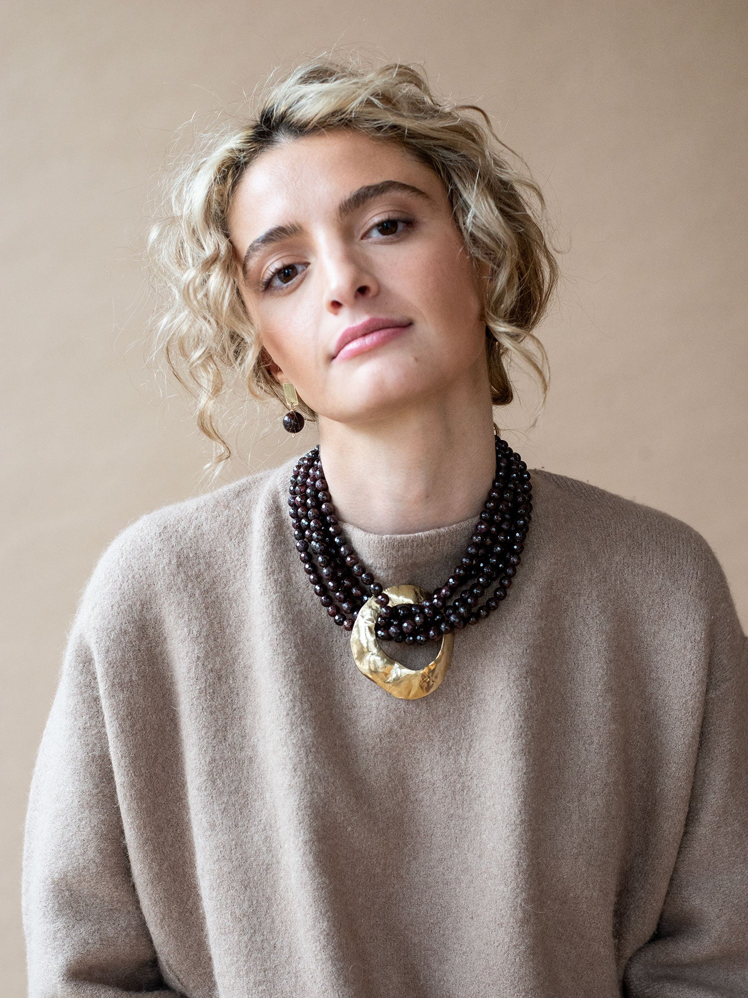 Multistrand beaded garnet necklace with a large central brass pendant by Michelle Ross