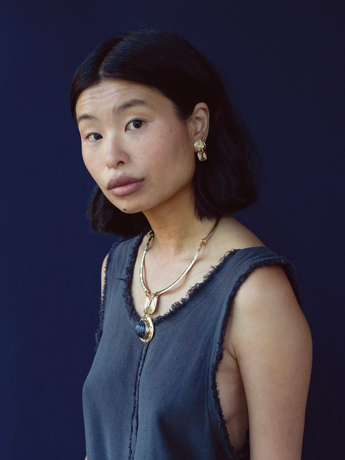 A woman wears a solid brass collar necklace with a lapis lazuli pendant by Canadian jewelry designer Michelle Ross