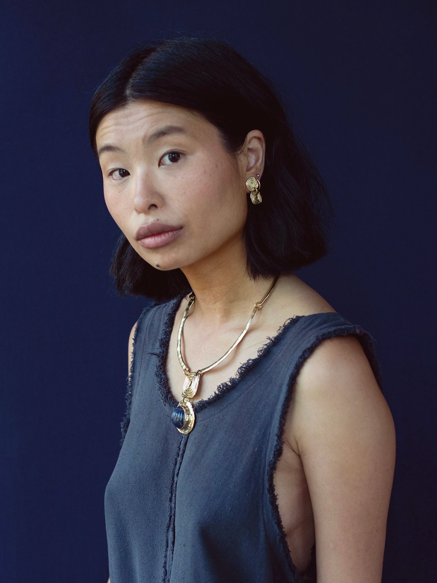 A woman wears a solid brass collar necklace with a lapis lazuli pendant by Canadian jewelry designer Michelle Ross