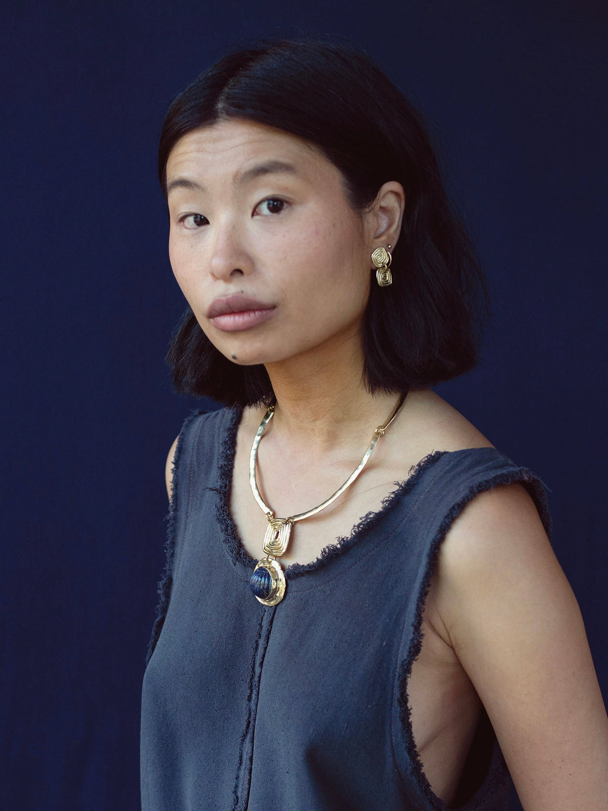 A woman wears a solid brass collar necklace with a lapis lazuli pendant by Canadian jewelry designer Michelle Ross