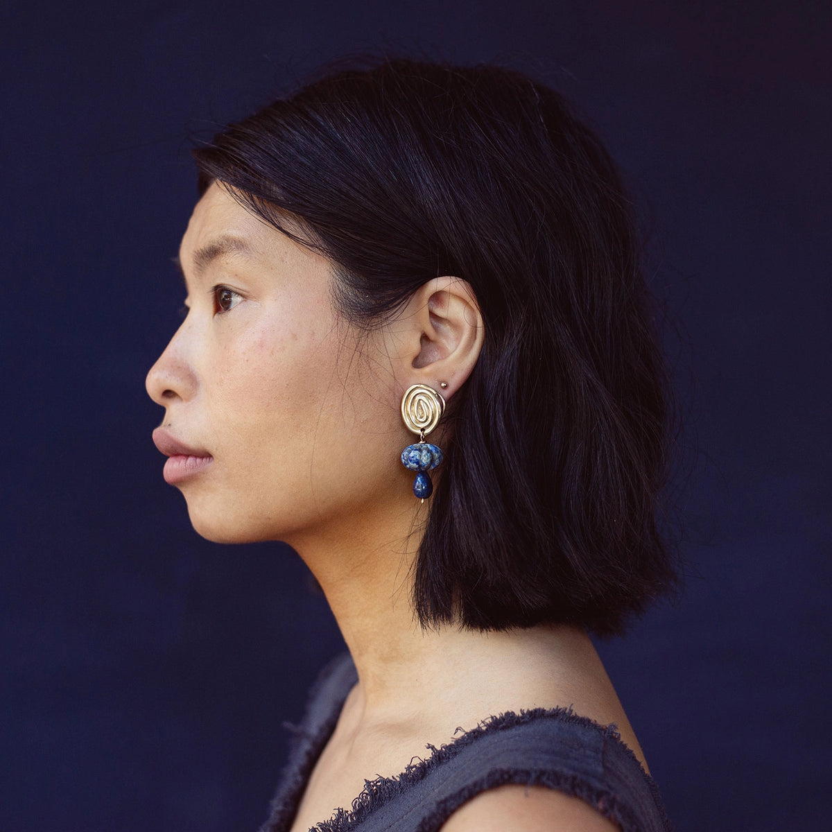 A woman wears a pair of hand-formed brass spiral earrings with lapis lazuli beaded stone drop style by Canadian jewelry designer Michelle Ross