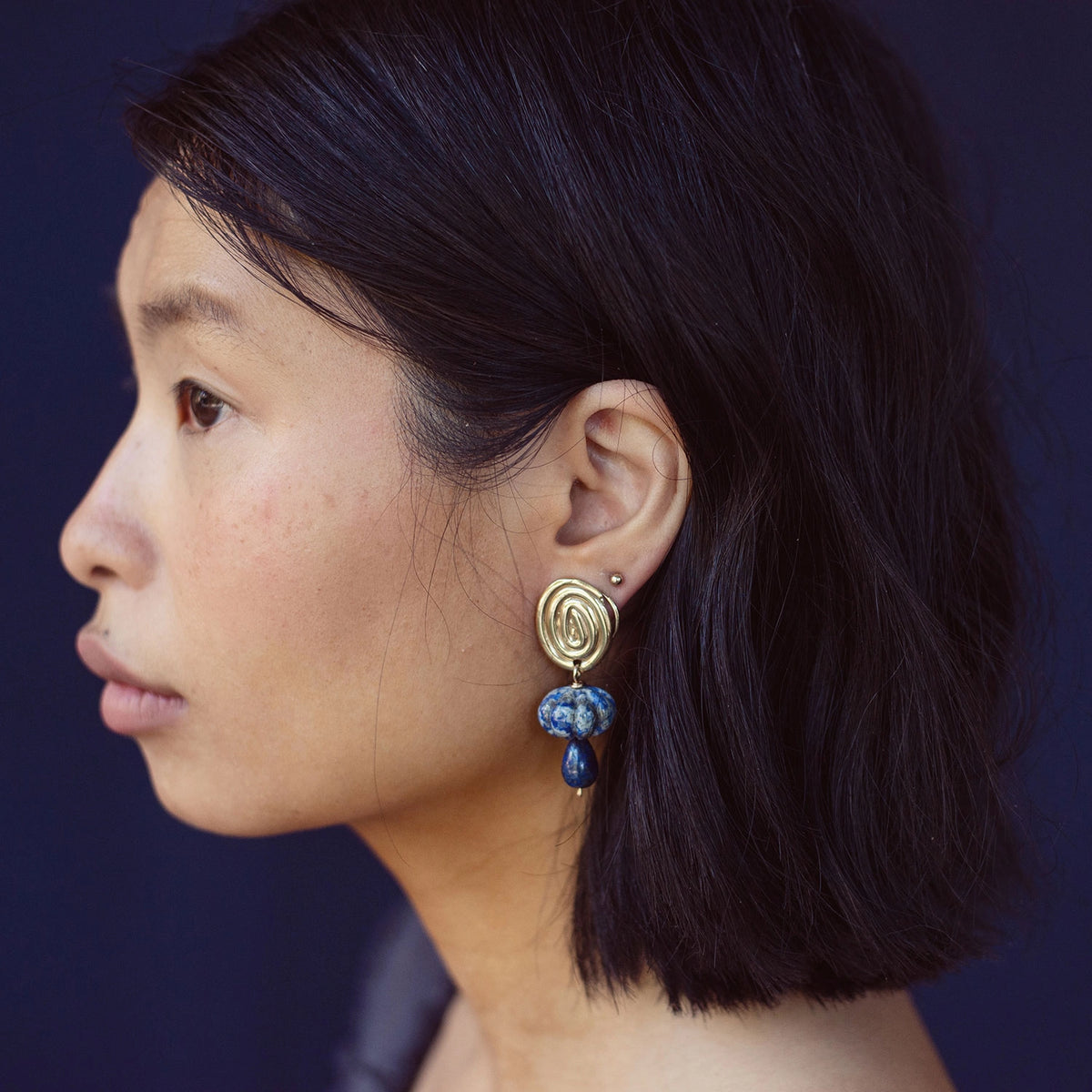 A woman wears a pair of hand-formed brass spiral earrings with lapis lazuli beaded stone drop style by Canadian jewelry designer Michelle Ross