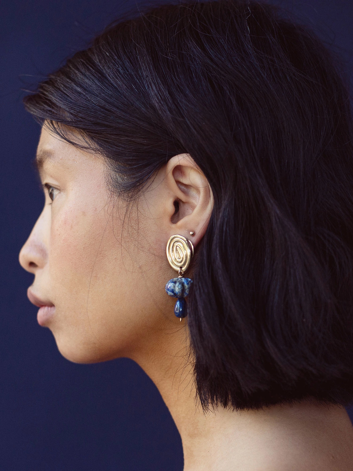A woman wears a pair of hand-formed brass spiral earrings with lapis lazuli beaded stone drop style by Canadian jewelry designer Michelle Ross