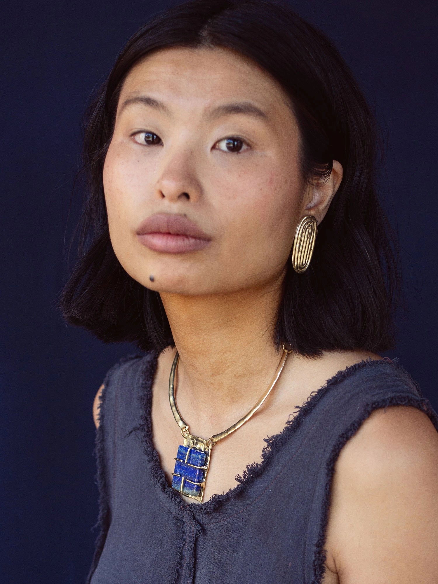 A woman wears a solid brass collar necklace with a lapis lazuli pendant by Canadian jewelry designer Michelle Ross