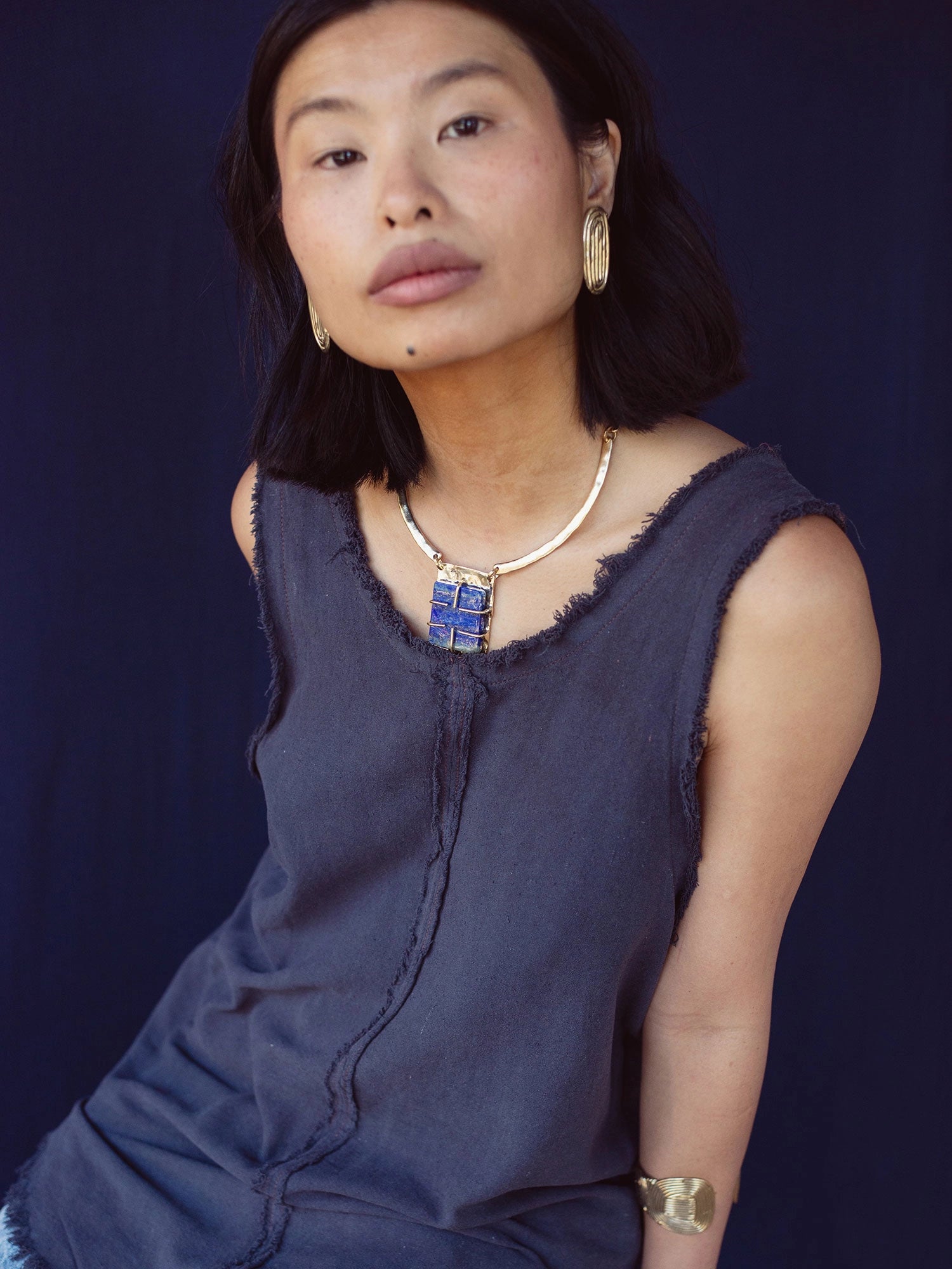 A woman wears a solid brass collar necklace with a lapis lazuli pendant by Canadian jewelry designer Michelle Ross