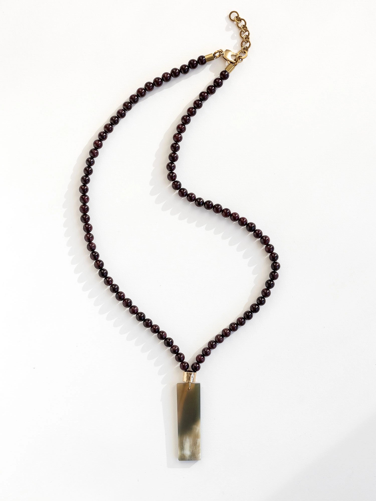 Necklace with small garnet beads and a large horn pendant with brass details by Michelle Ross