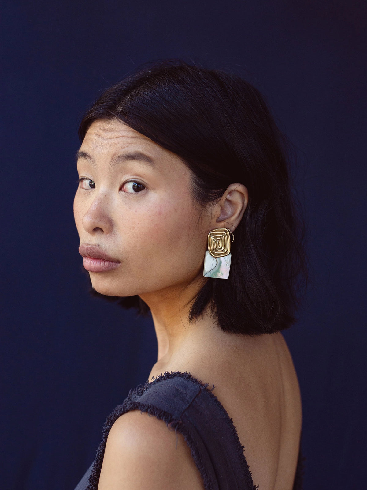 A woman wears a pair of brass spiral earrings with square shell drops by Canadian jewelry designer Michelle Ross 