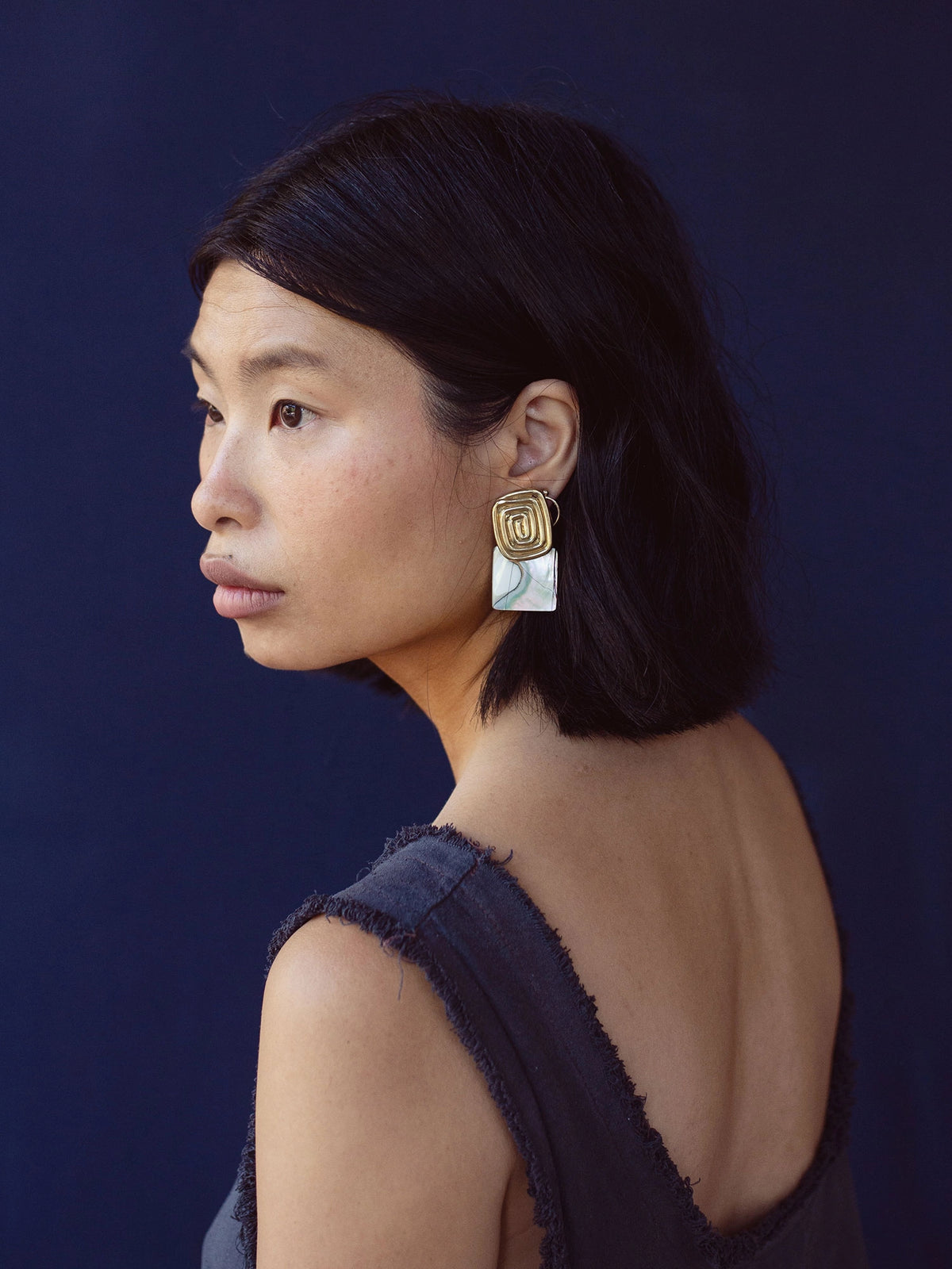 A woman wears a pair of brass spiral earrings with square shell drops by Canadian jewelry designer Michelle Ross 