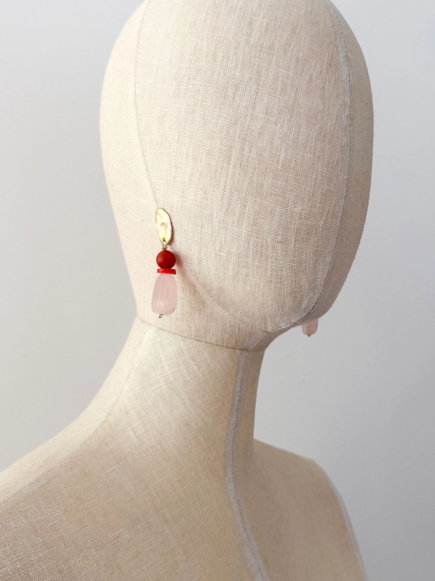 A pair of statement dangle earrings featuring textured brass tops, a round red carnelian bead, a small coral spacer, and a teardrop-shaped pale pink rose quartz bead by Canadian jewelry designer Michelle Ross.