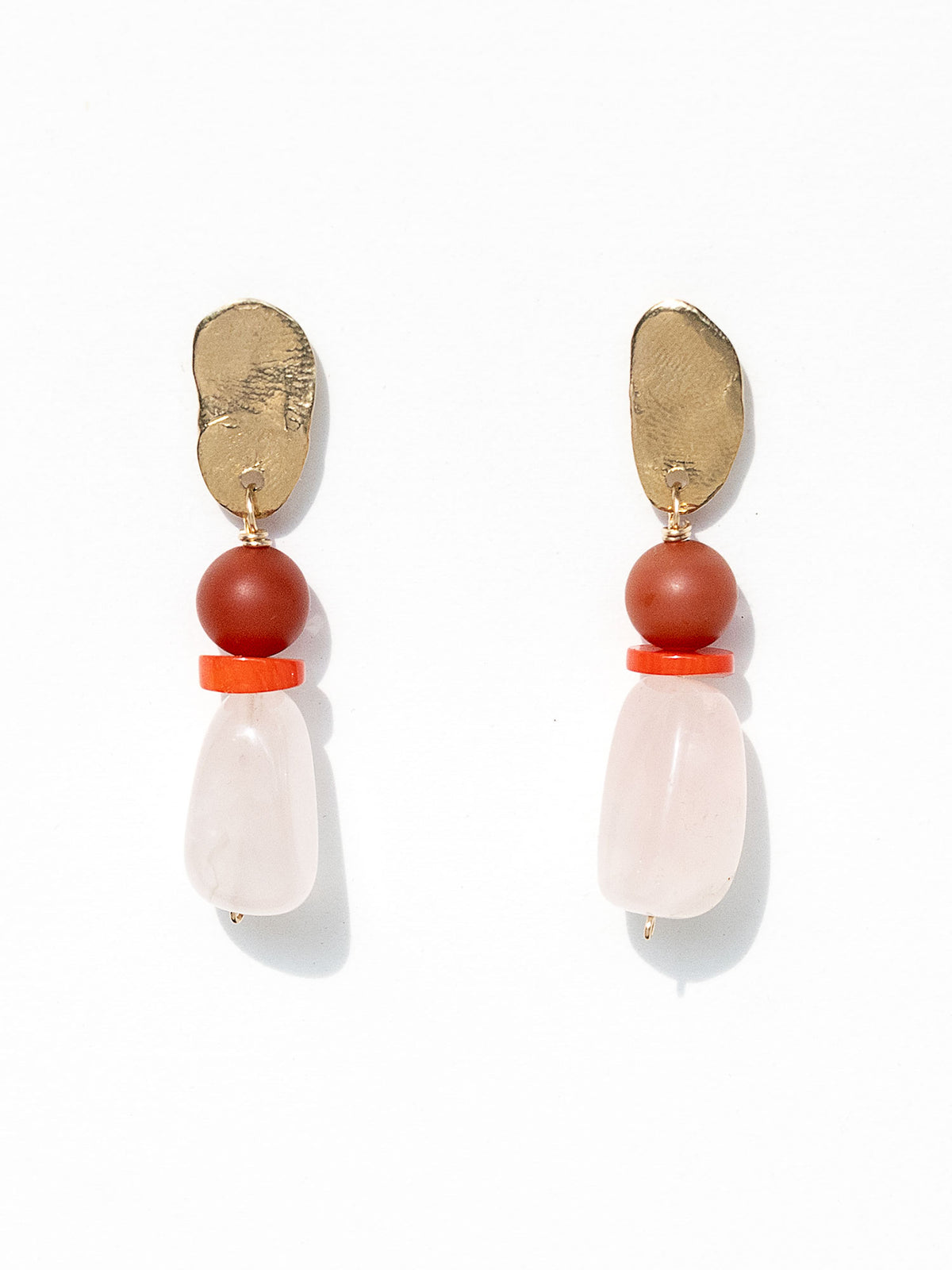A pair of statement dangle earrings featuring textured brass tops, a round red carnelian bead, a small coral spacer, and a teardrop-shaped pale pink rose quartz bead by Canadian jewelry designer Michelle Ross.