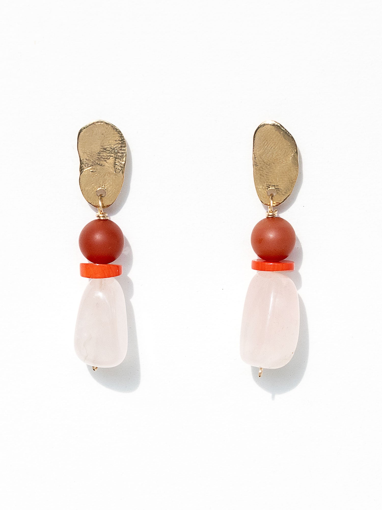 A pair of statement dangle earrings featuring textured brass tops, a round red carnelian bead, a small coral spacer, and a teardrop-shaped pale pink rose quartz bead by Canadian jewelry designer Michelle Ross.