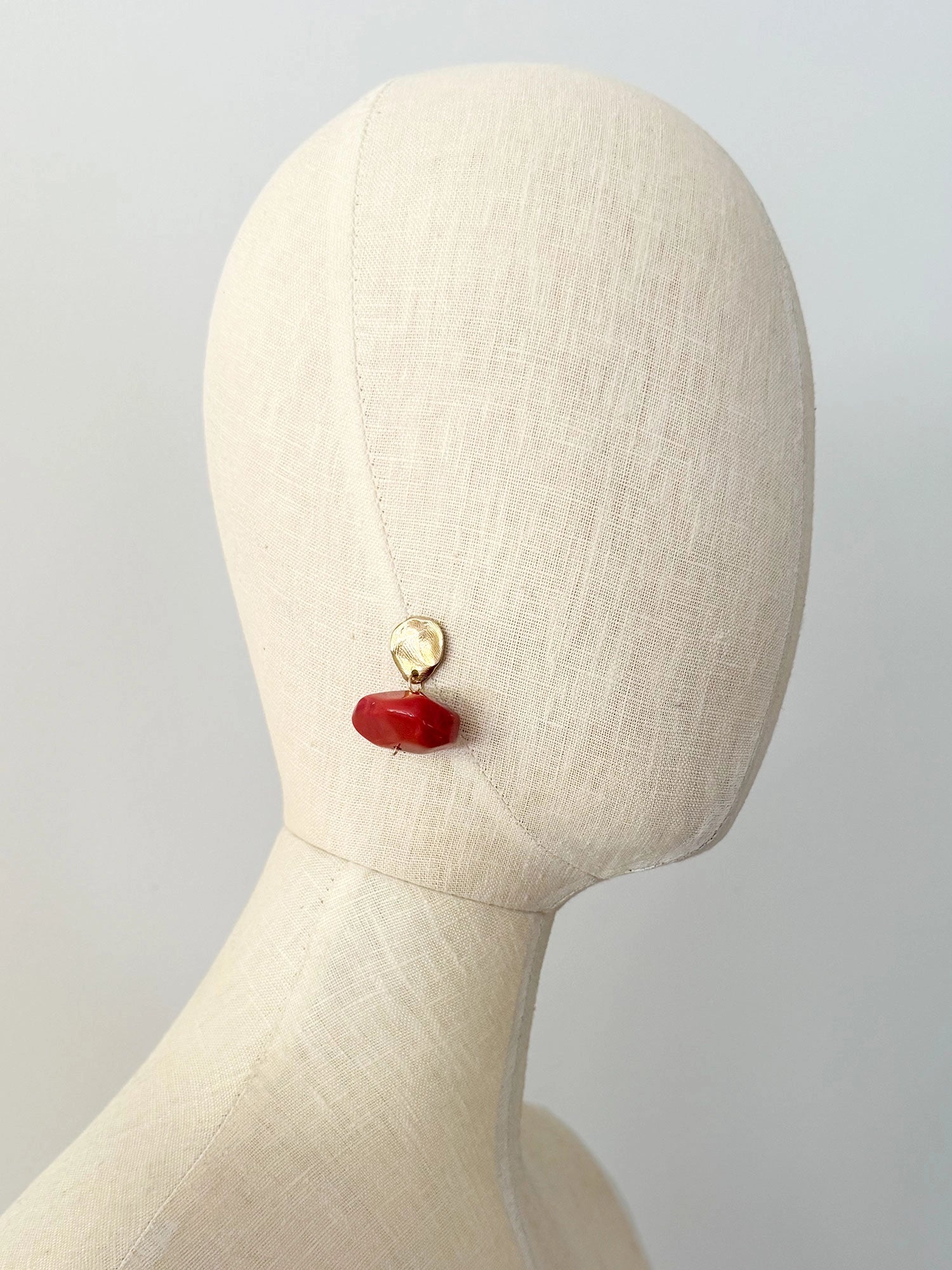 A pair of drop earrings featuring textured brass metal studs and large, polished red resin beaded drops by Canadian jewelry designer Michelle Ross