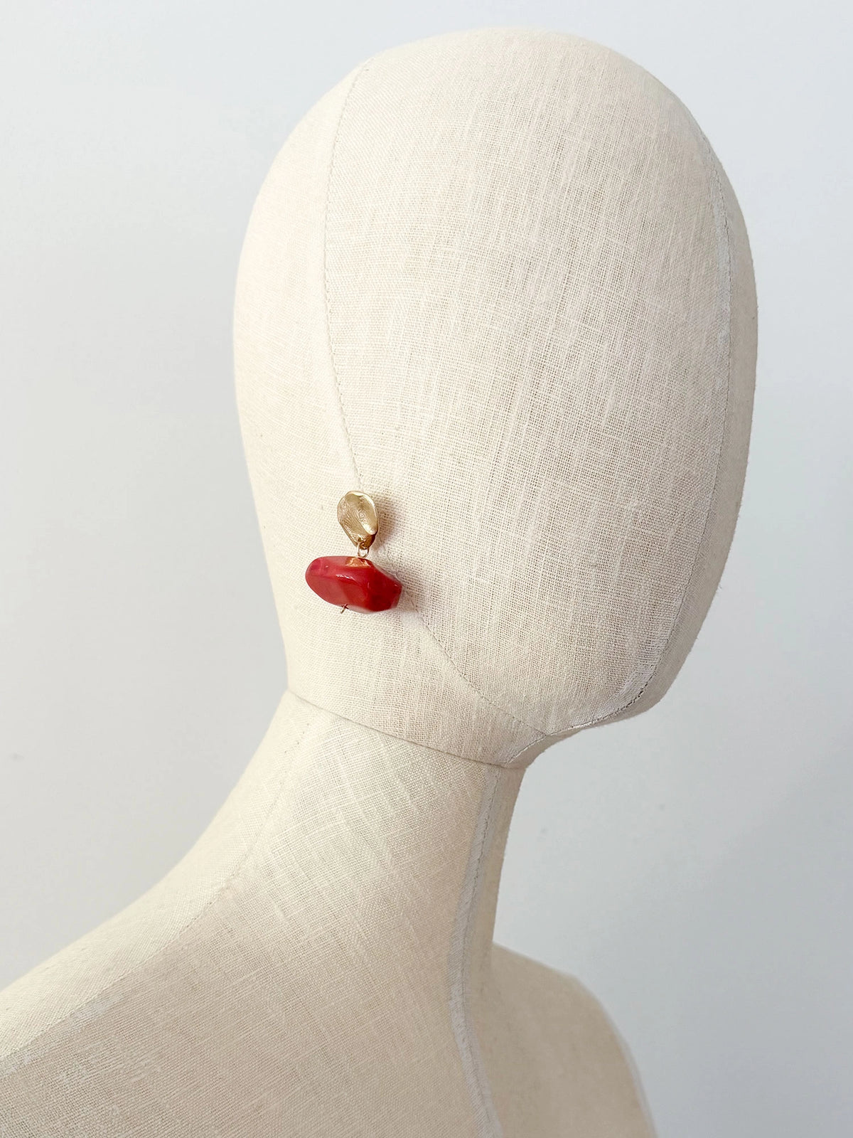 A pair of drop earrings featuring textured brass metal studs and large, polished red resin beaded drops by Canadian jewelry designer Michelle Ross