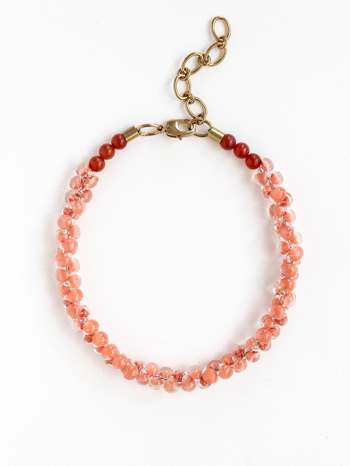 A beaded short necklace featuring a gradient of translucent peach and coral pink glass beads transitioning to dark red carnelian beads near the clasp, finished with brass metal hardware.