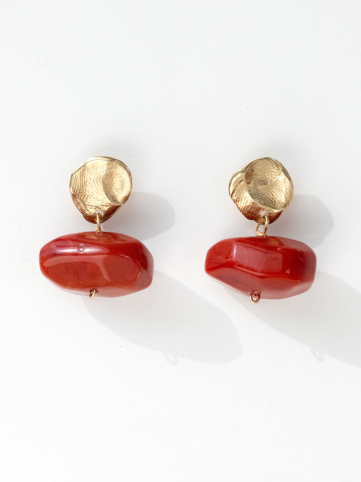 A pair of drop earrings featuring textured brass metal studs and large, polished red resin beaded drops by Canadian jewelry designer Michelle Ross