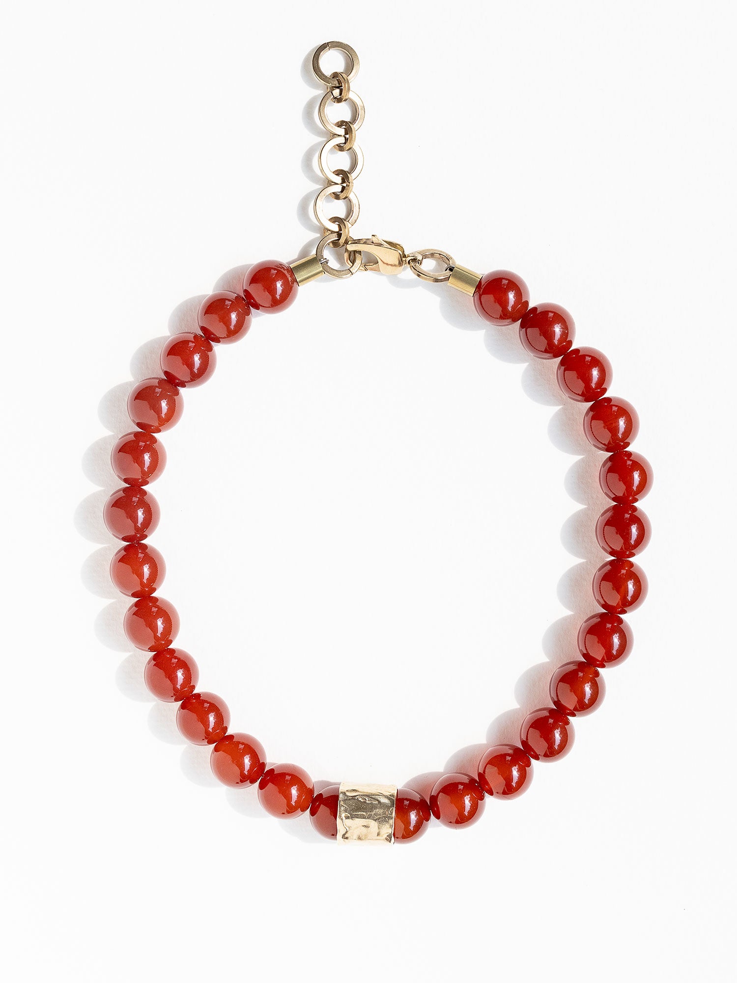 A beaded necklace featuring glossy red round carnelian beads and a textured brass accent piece by Canadian jewelry designer Michelle Ross