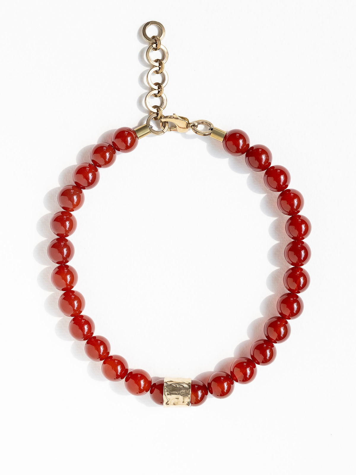 A beaded necklace featuring glossy red round carnelian beads and a textured brass accent piece by Canadian jewelry designer Michelle Ross