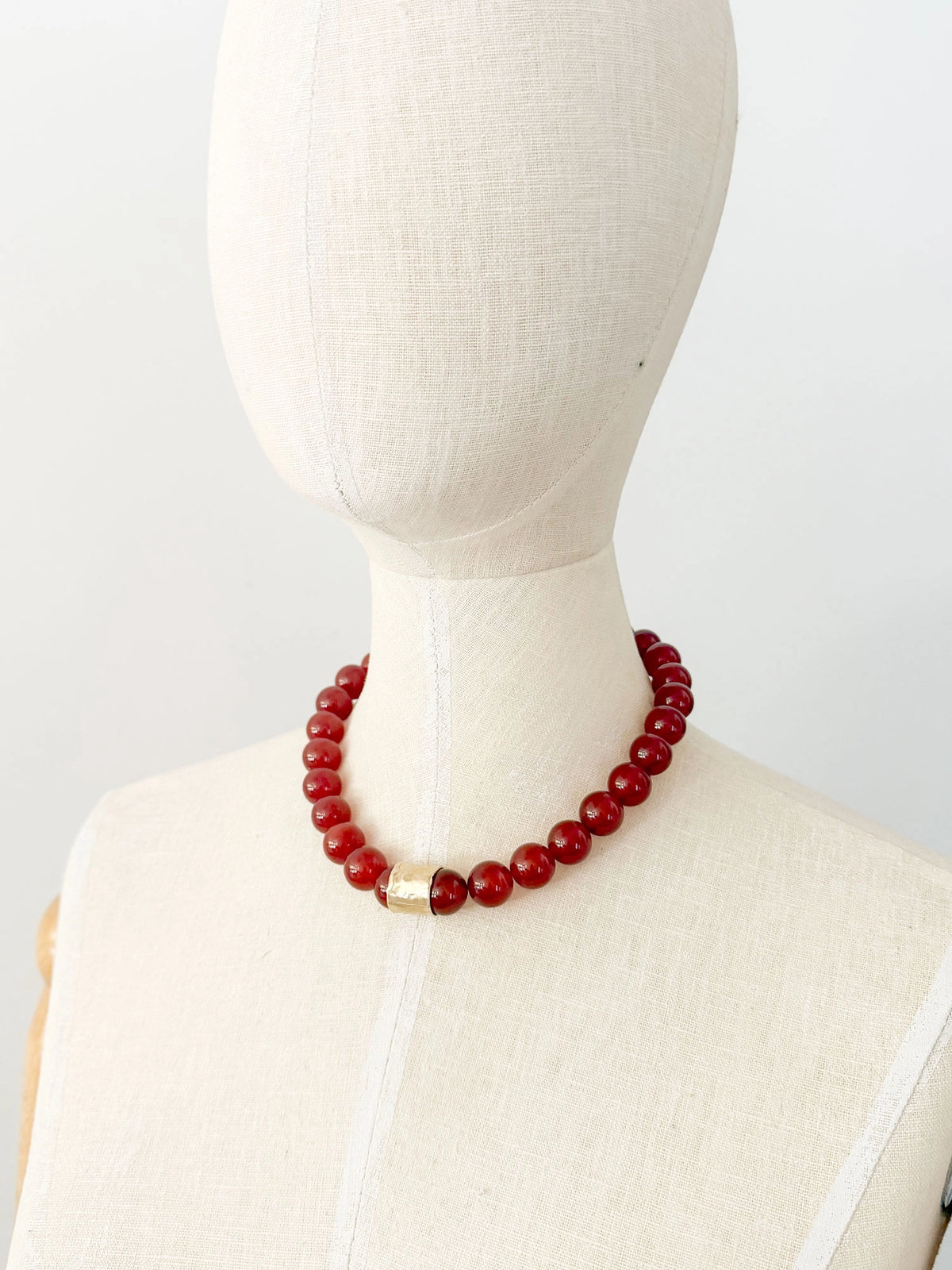 A beaded necklace featuring glossy red round carnelian beads and a textured brass accent piece by Canadian jewelry designer Michelle Ross