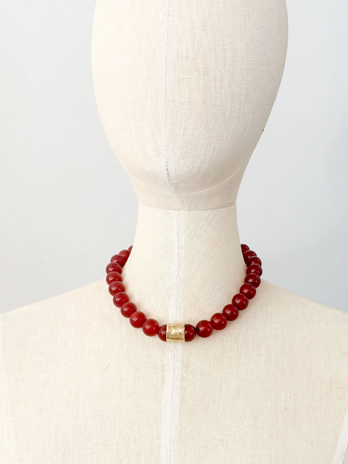 A beaded necklace featuring glossy red round carnelian beads and a textured brass accent piece by Canadian jewelry designer Michelle Ross