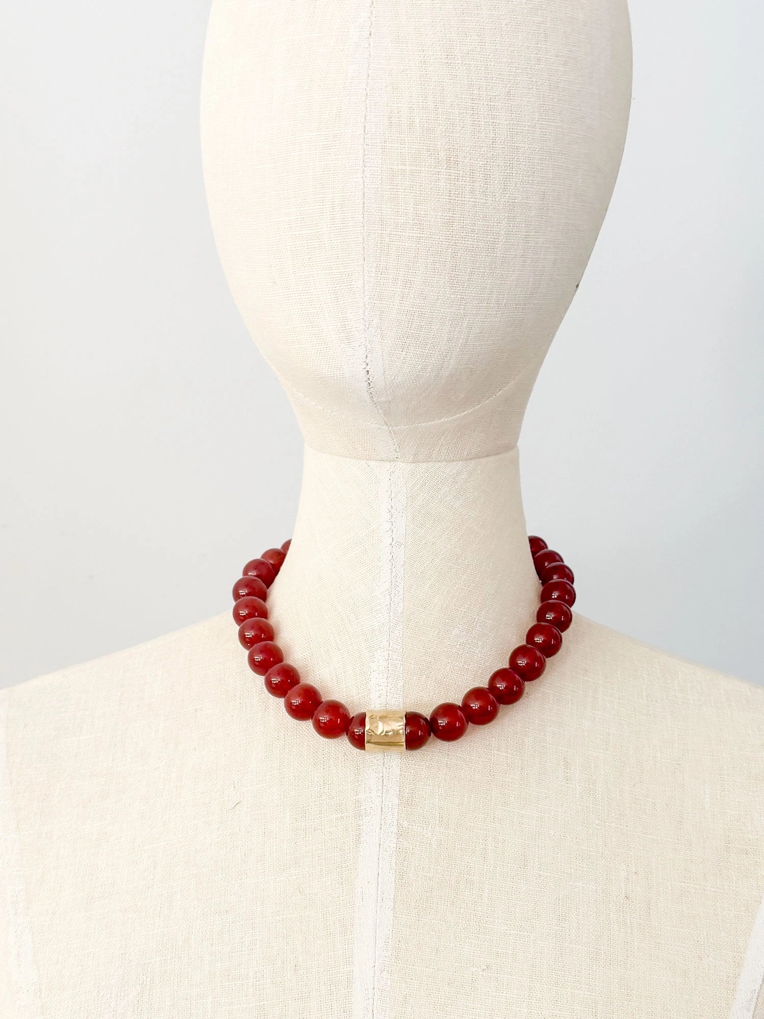 A beaded necklace featuring glossy red round carnelian beads and a textured brass accent piece by Canadian jewelry designer Michelle Ross