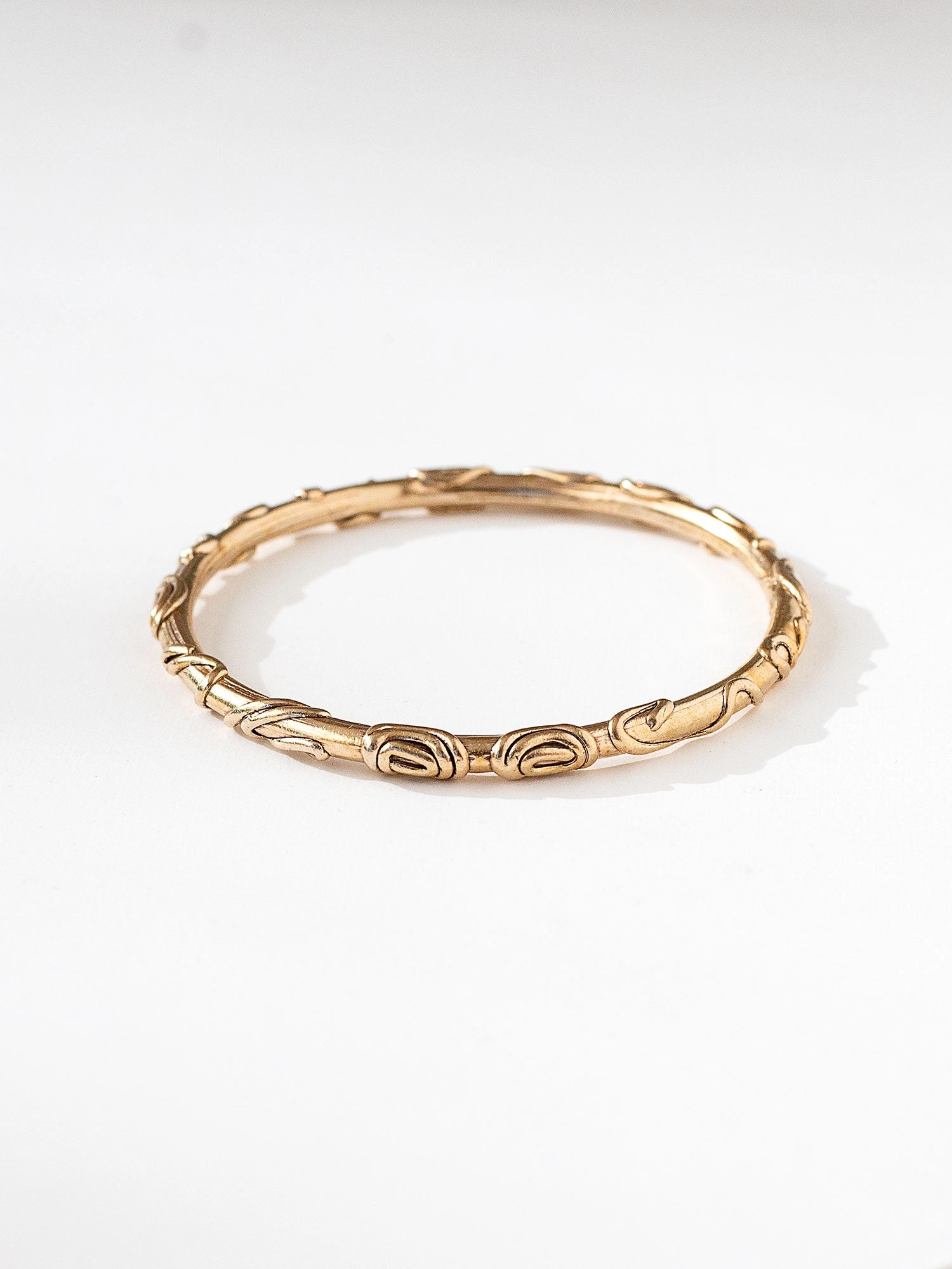 A solid brass bangle bracelet with spiral scrollwork details by contemporary jewelry designer Michelle Ross