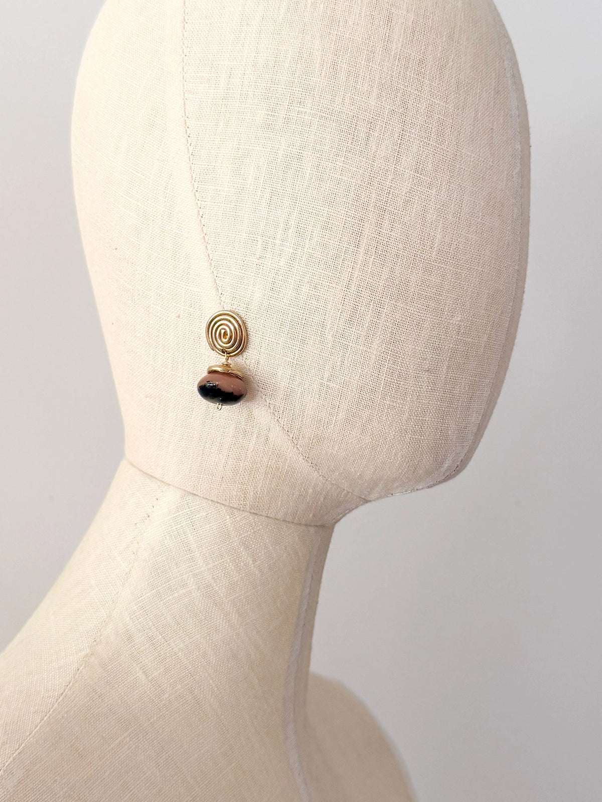 A pair of brass spiral drop earrings with marbled pink and black beads hanging below by Canadian jewelry designer Michelle Ross