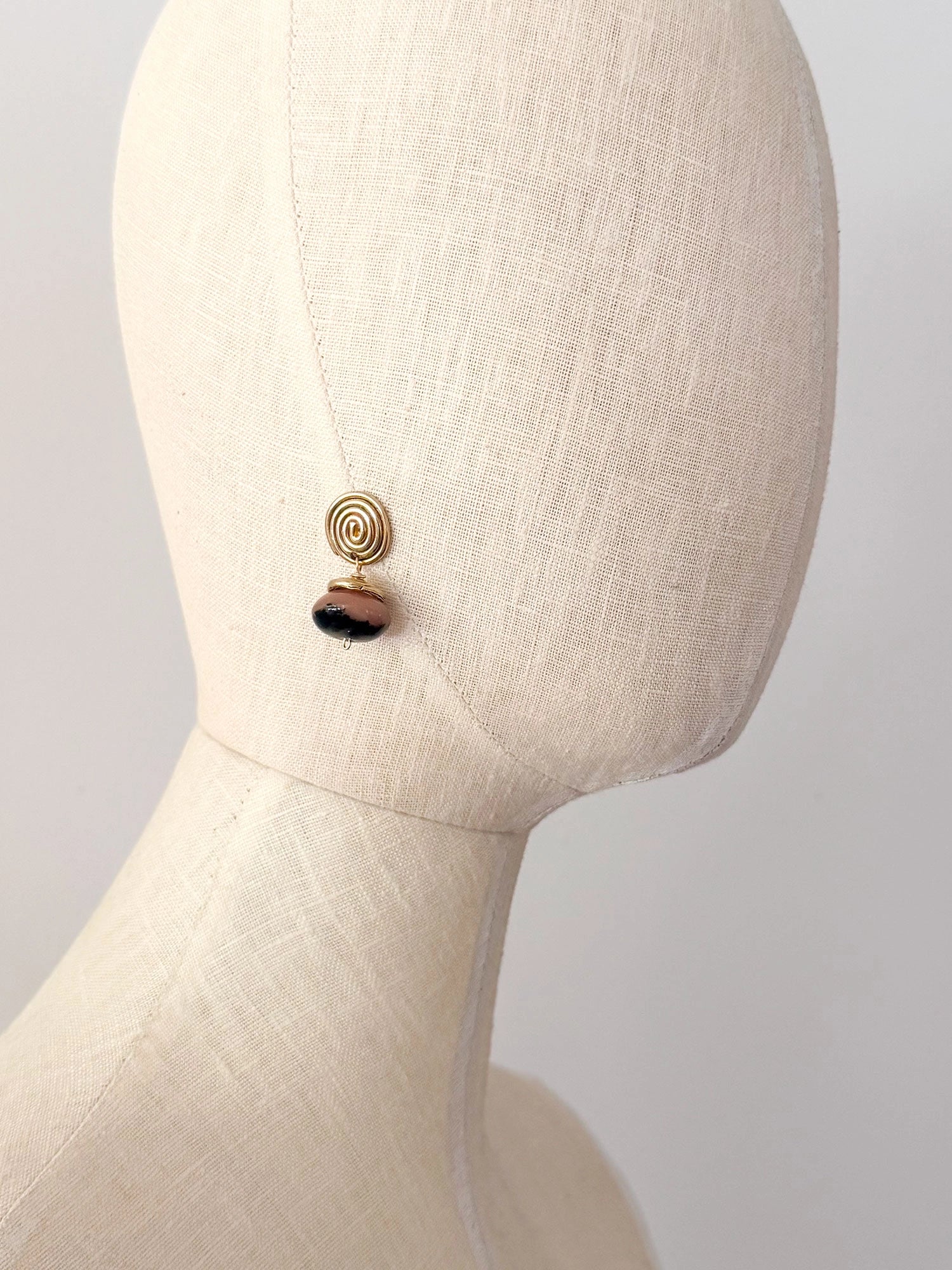 A pair of brass spiral drop earrings with marbled pink and black beads hanging below by Canadian jewelry designer Michelle Ross