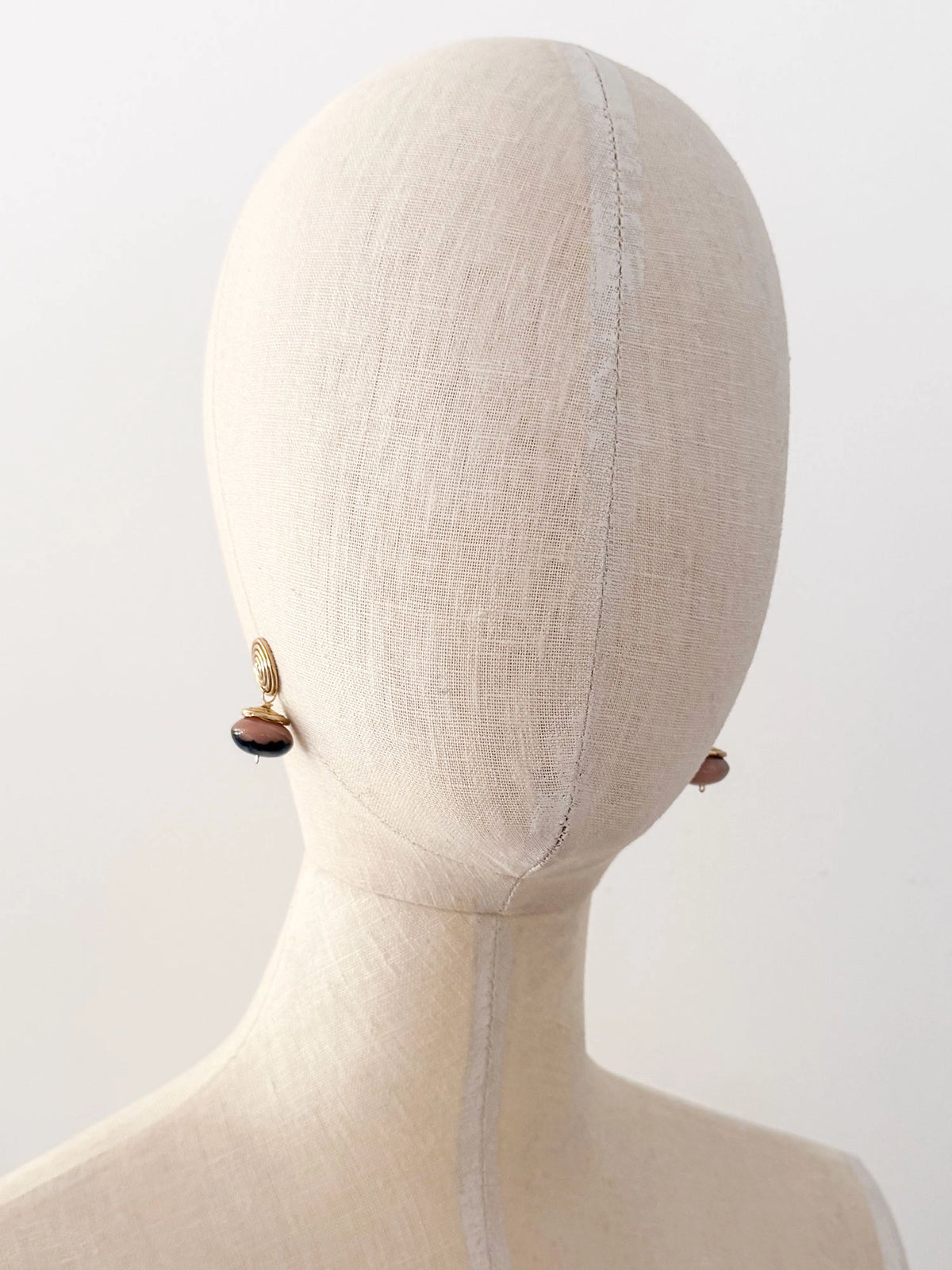 A pair of brass spiral drop earrings with marbled pink and black beads hanging below by Canadian jewelry designer Michelle Ross