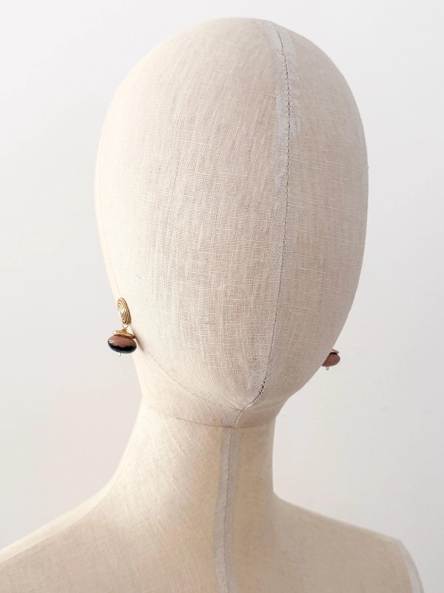 A pair of brass spiral drop earrings with marbled pink and black beads hanging below by Canadian jewelry designer Michelle Ross