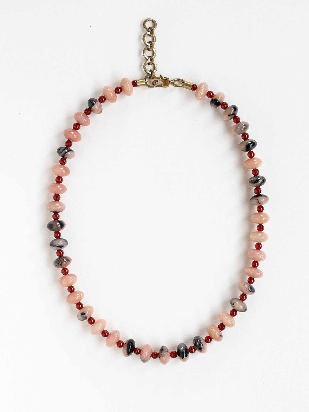 A beaded necklace featuring light pink and grey marbled stone beads, dark red round beads, finished with an antique brass clasp.