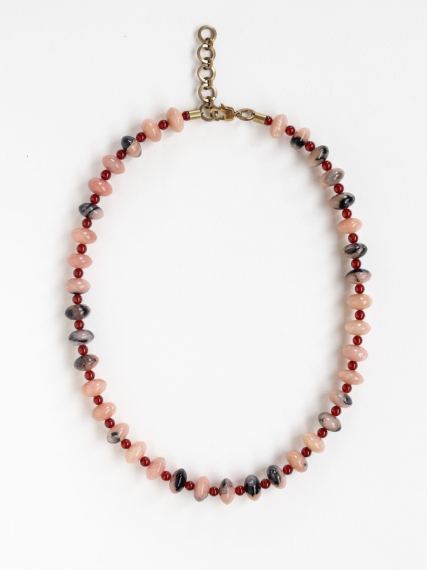 A beaded necklace featuring light pink and grey marbled stone beads, dark red round beads, finished with an antique brass clasp.