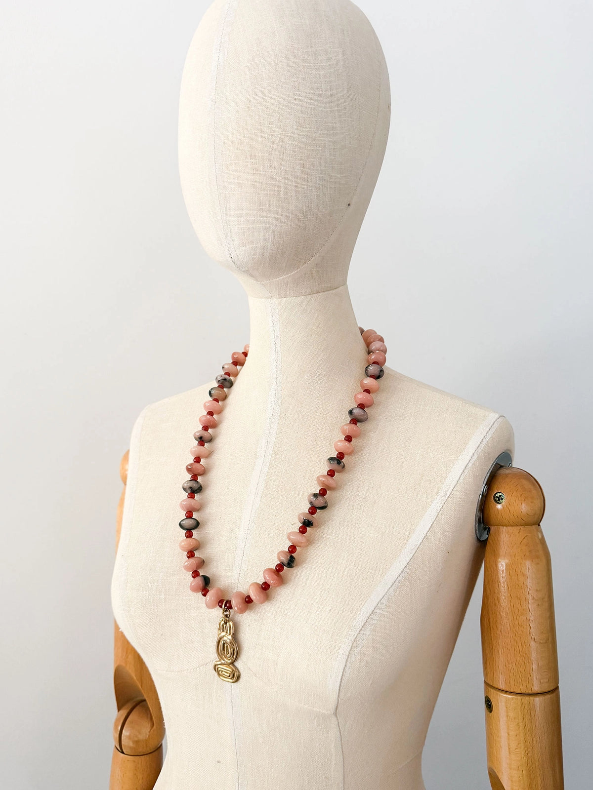 A beaded necklace featuring light pink stone with grey marbled beads, dark red beads, accented with a brass metal clasp by Canadian jewelry designer Michelle Ross