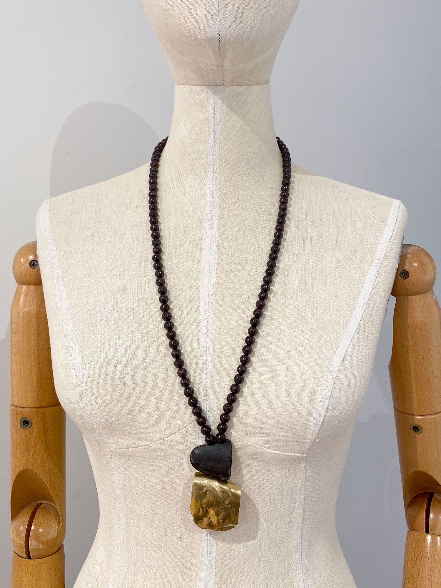 Necklace with garnet beads and a brass pendant by Canadian designer Michelle Ross