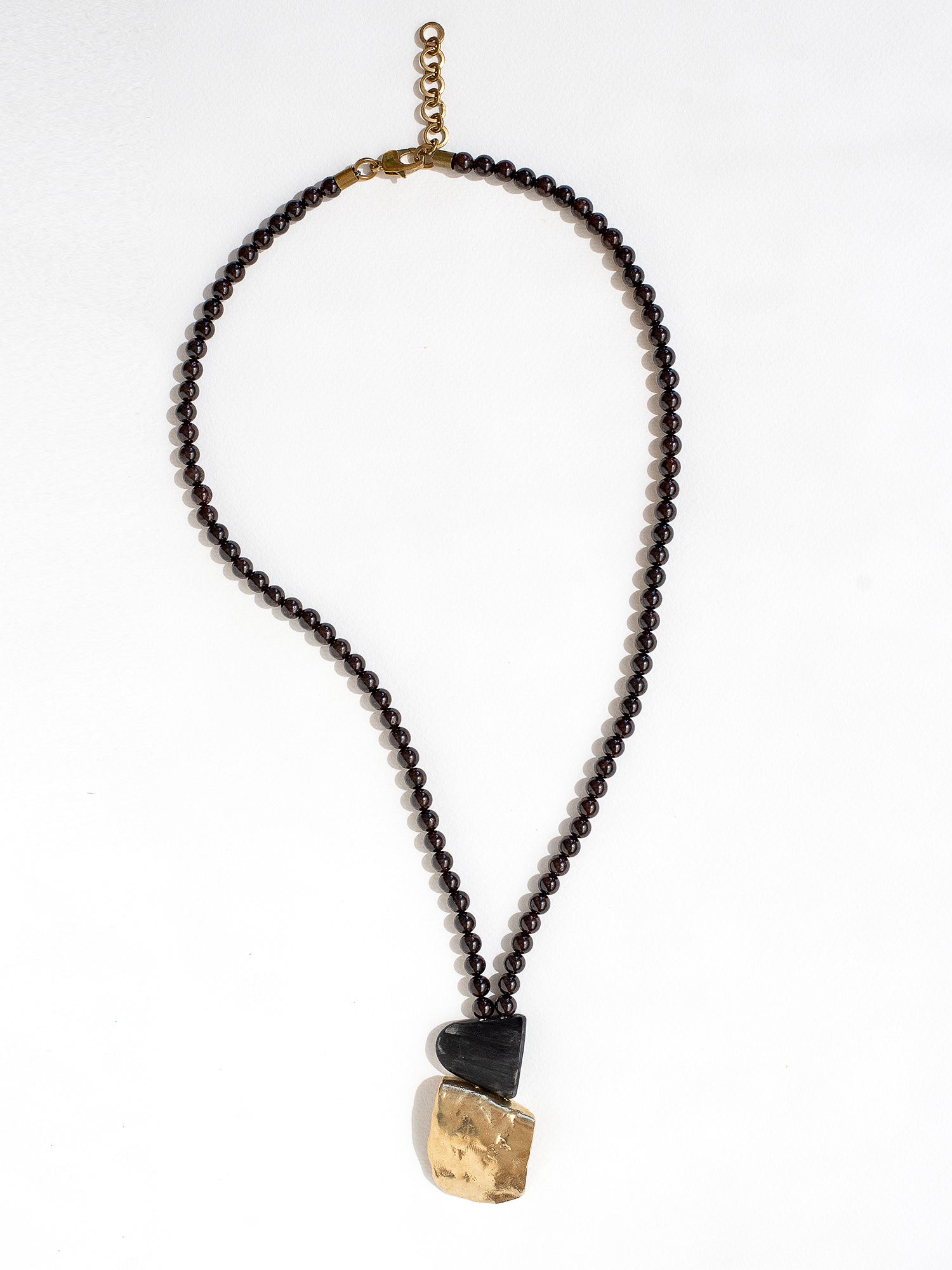 Necklace with garnet beads and a brass pendant by Canadian designer Michelle Ross