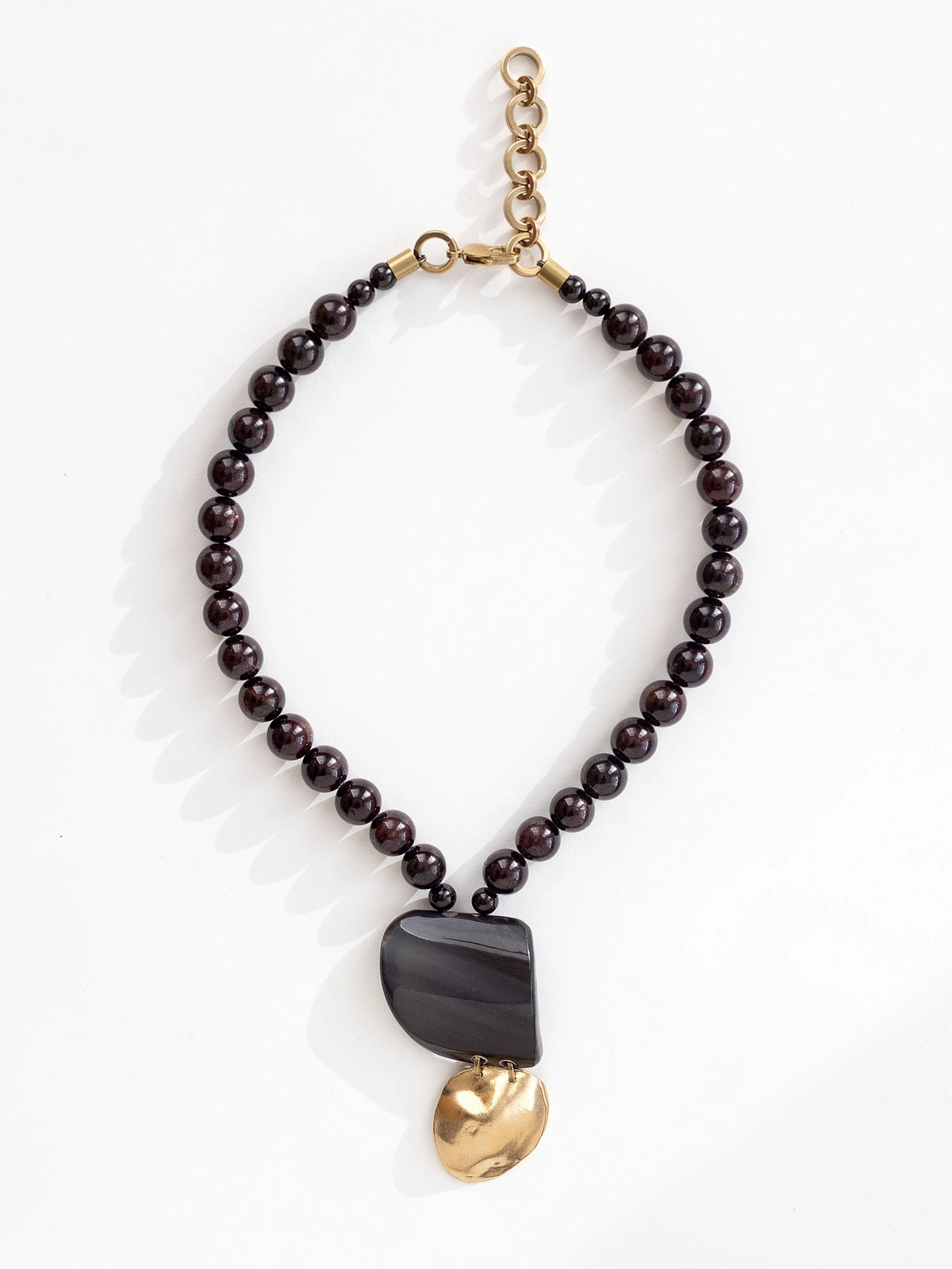 Necklace with garnet beads and a large black horn and brass pendant by Michelle Ross