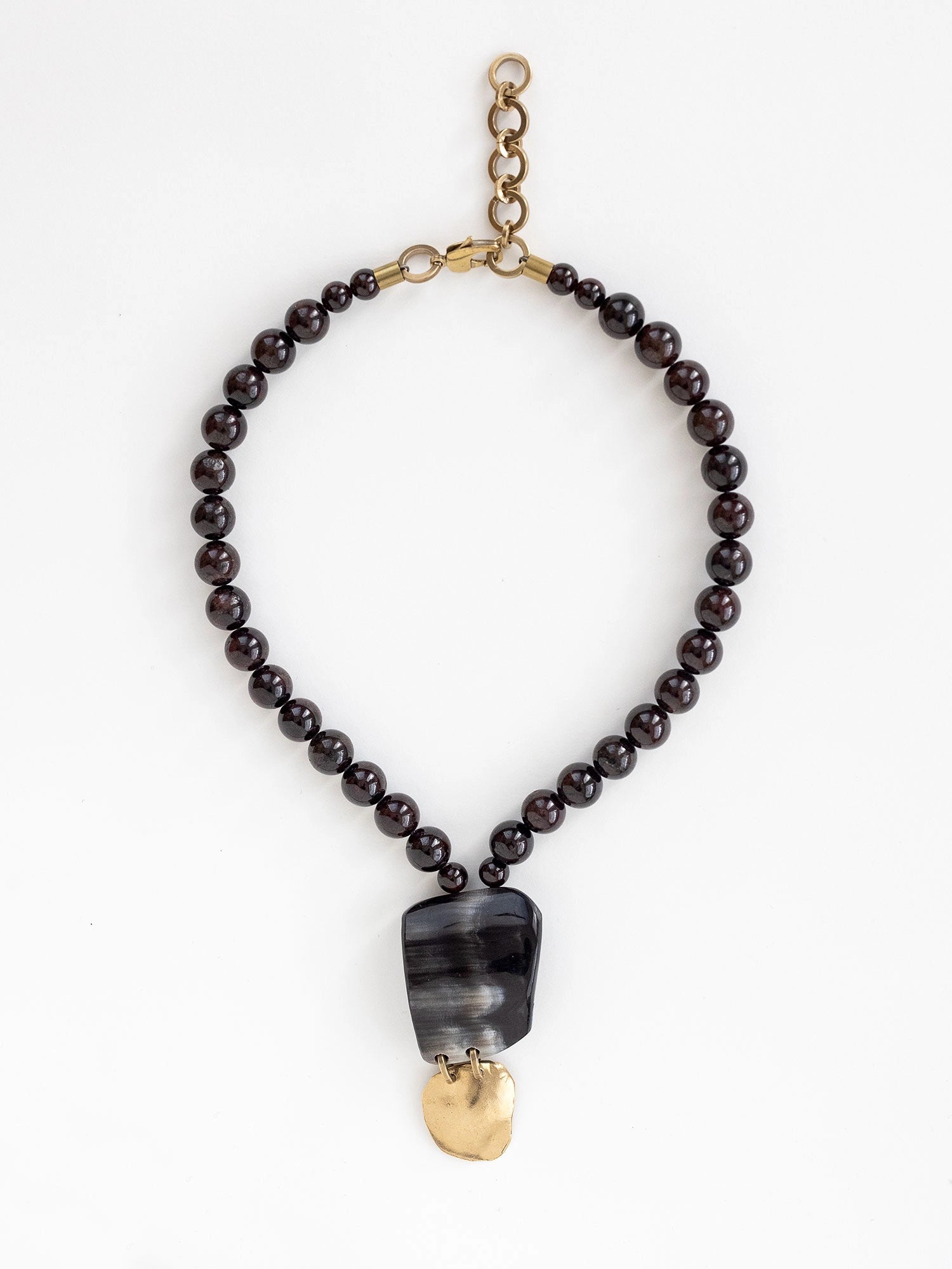 Necklace with garnet beads and a large black horn and brass pendant by Michelle Ross