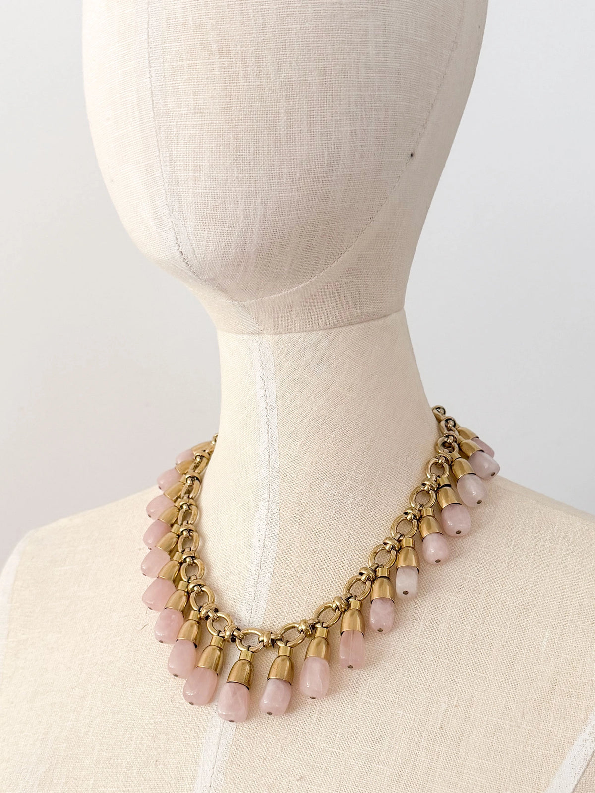 A statement collar necklace featuring a brass chain and links with dangling rose quartz beads by Canadian designer Michelle Ross