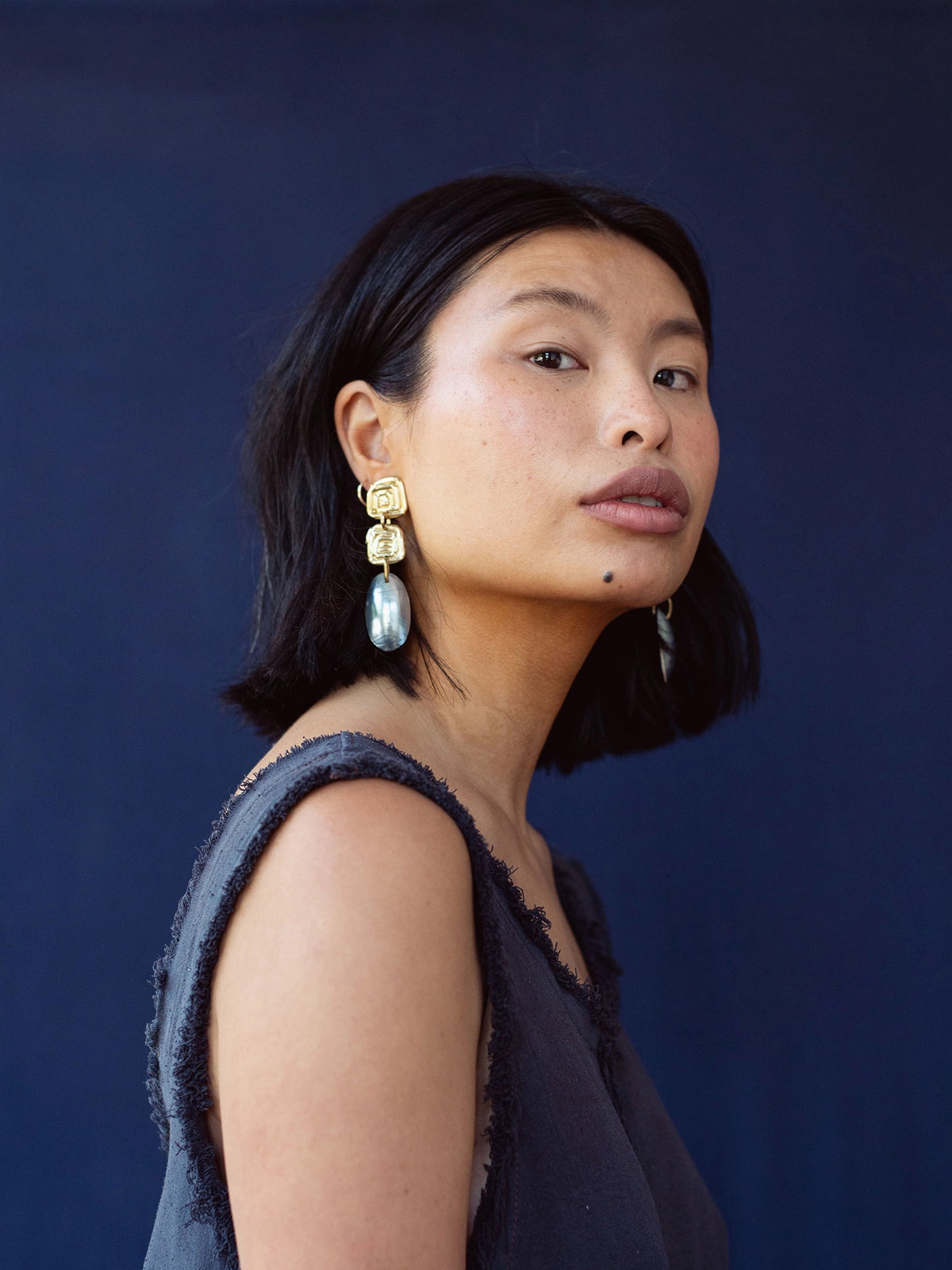 A woman wears statement earrings with a handmade brass spiral design and blue shell drop by Canadian jewelry designer Michelle Ross