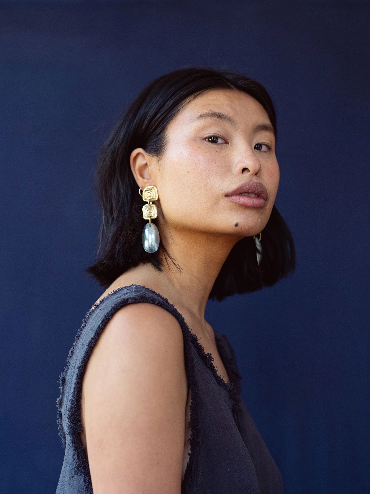 A woman wears statement earrings with a handmade brass spiral design and blue shell drop by Canadian jewelry designer Michelle Ross