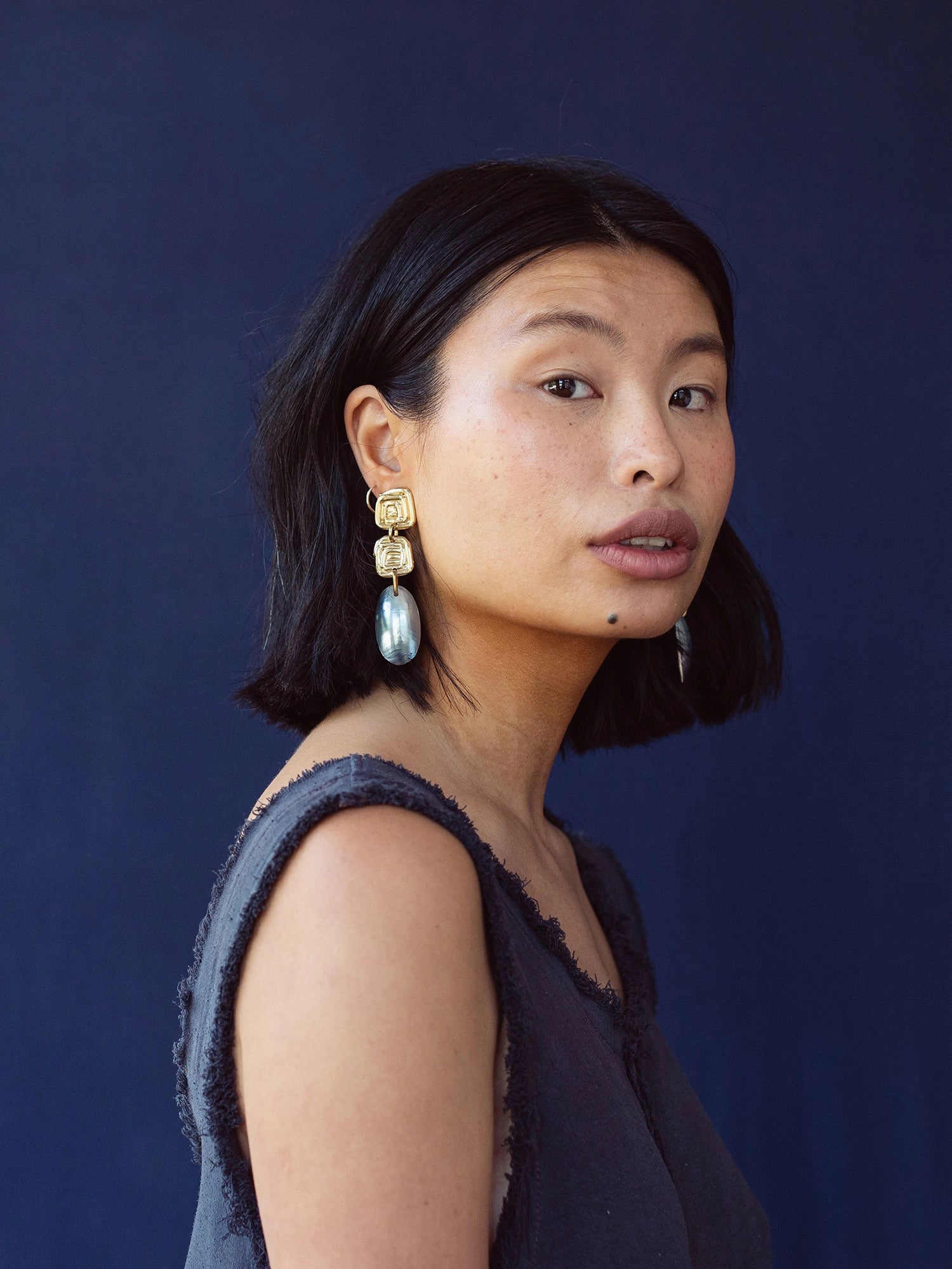 A woman wears statement earrings with a handmade brass spiral design and blue shell drop by Canadian jewelry designer Michelle Ross