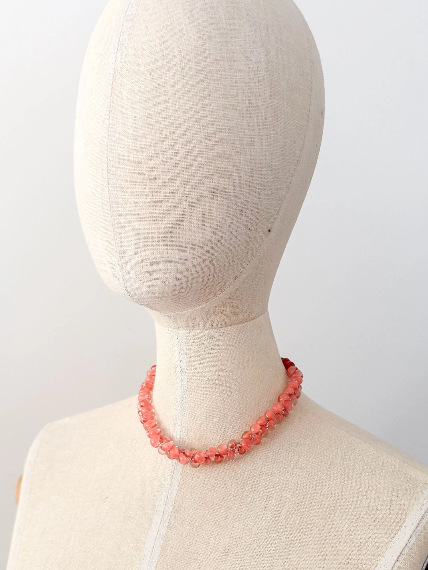 A beaded short necklace featuring a gradient of translucent peach and coral pink glass beads transitioning to dark red carnelian beads near the clasp, finished with brass metal hardware.