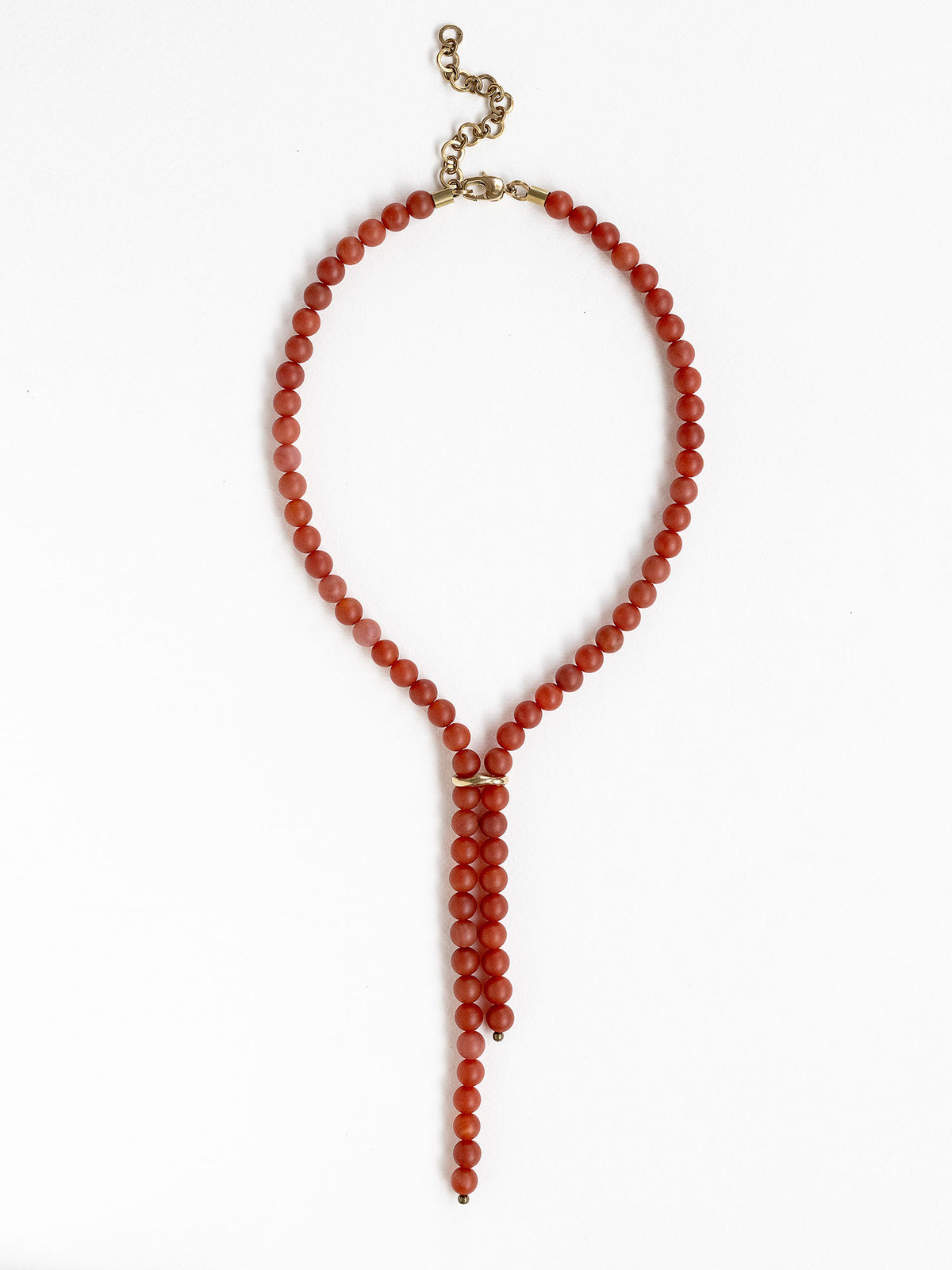 A beaded lariat style necklace made of round carnelian red beads with brass details by Canadian jewelry designer Michelle Ross