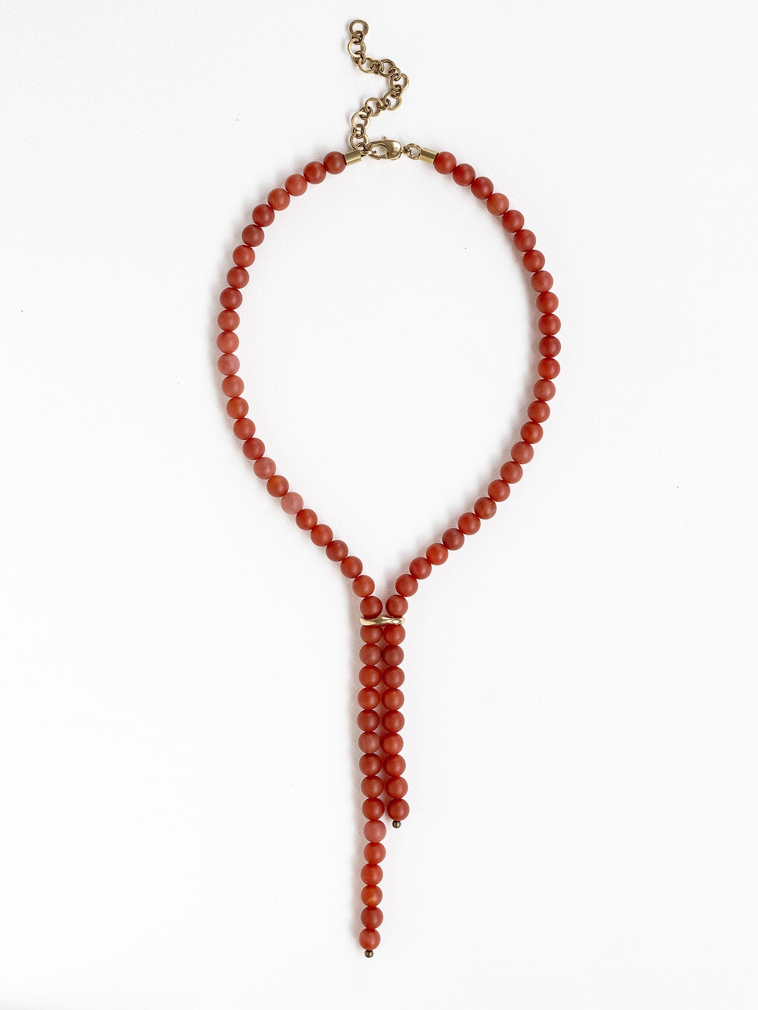 A beaded lariat style necklace made of round carnelian red beads with brass details by Canadian jewelry designer Michelle Ross