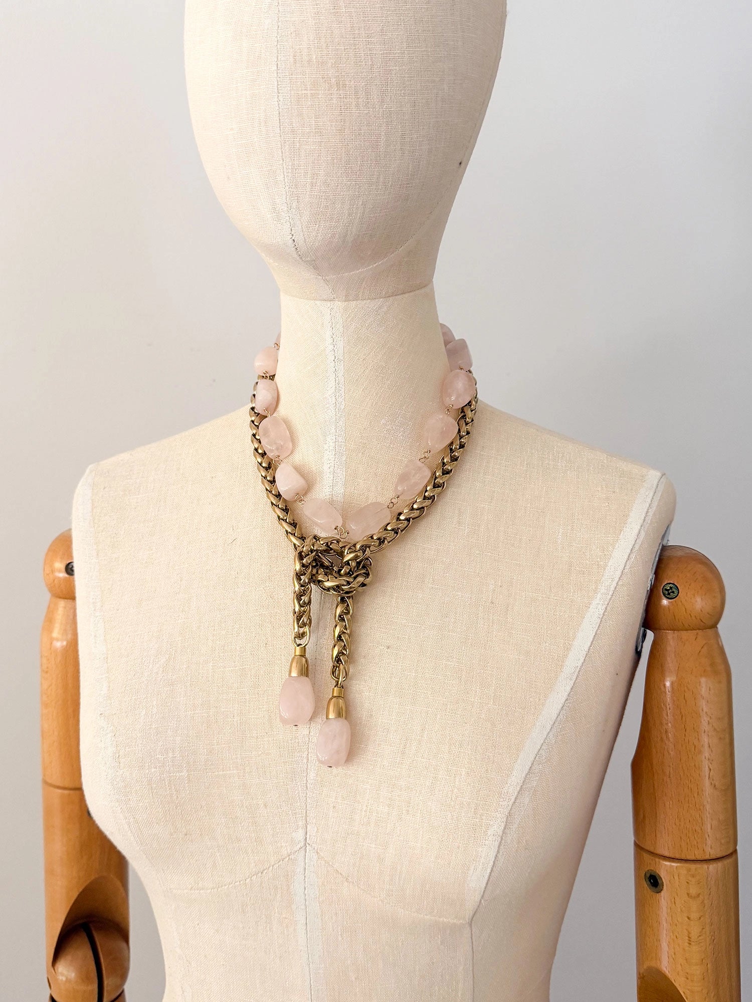 A brass chain lariat necklace knotted with two dangling light pink rose quartz teardrop-shaped beads at the bottom with a beaded rose quartz necklace layered over top by Canadian jewelry designer Michelle Ross