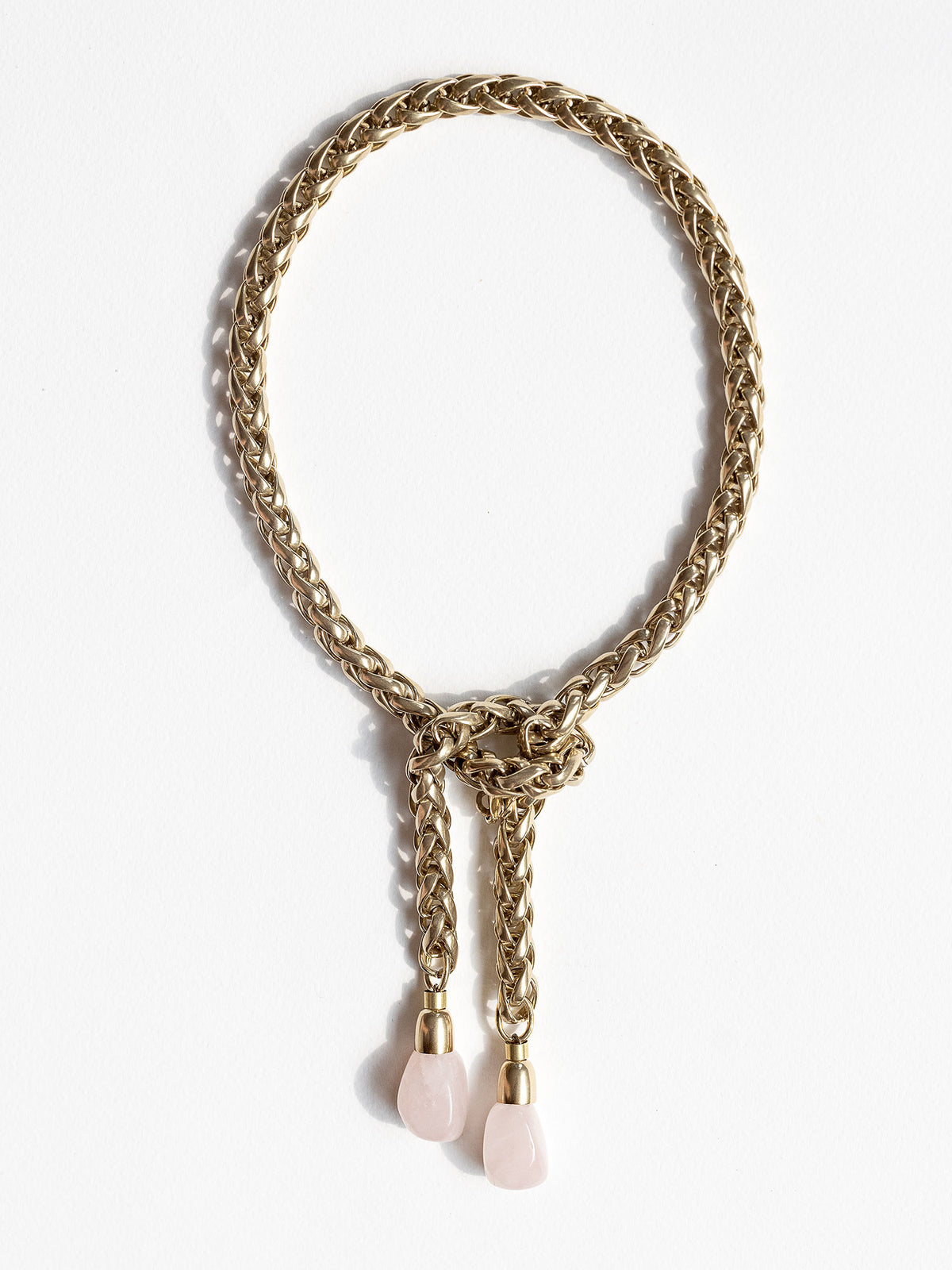 A brass chain lariat necklace knotted with two dangling light pink rose quartz teardrop-shaped beads at the bottom by Canadian jewelry designer Michelle Ross