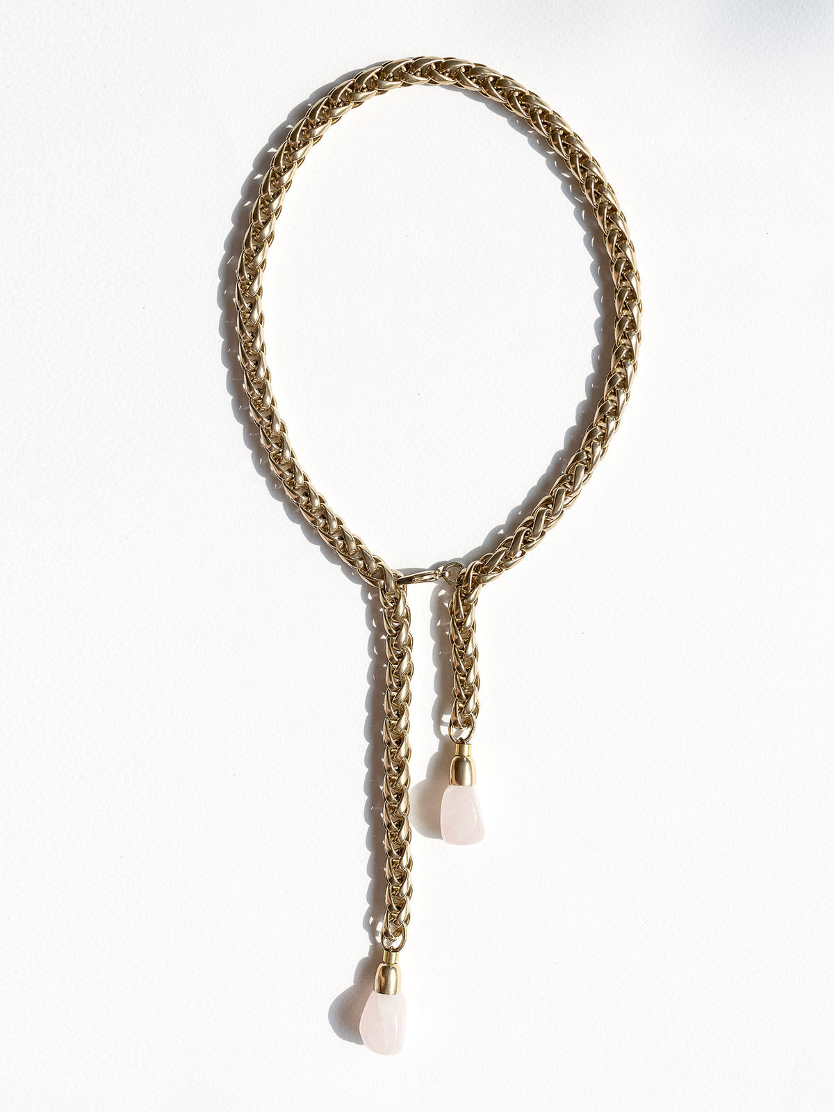 A brass chain lariat necklace knotted with two dangling light pink rose quartz teardrop-shaped beads at the bottom by Canadian jewelry designer Michelle Ross