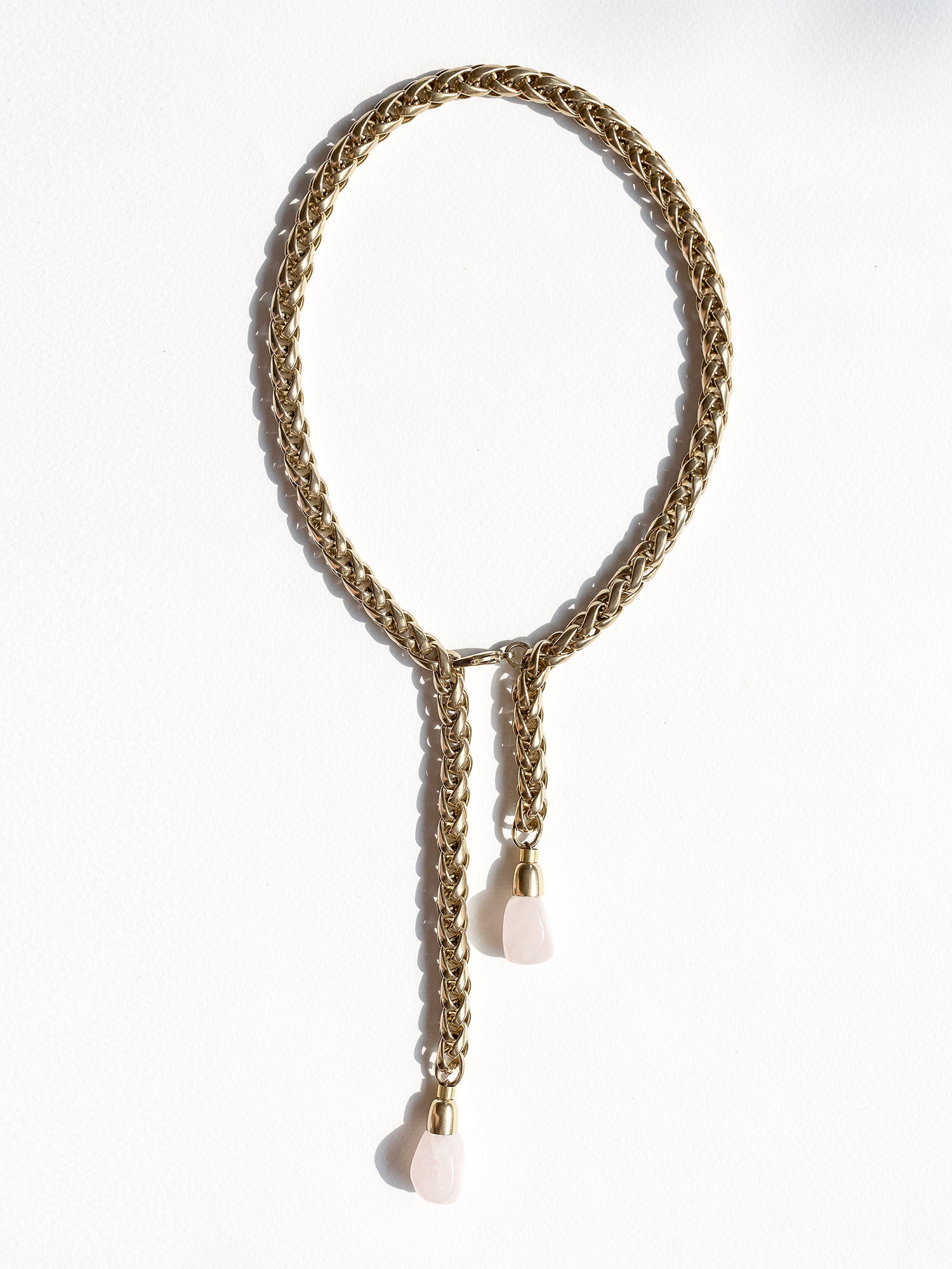 A brass chain lariat necklace knotted with two dangling light pink rose quartz teardrop-shaped beads at the bottom by Canadian jewelry designer Michelle Ross