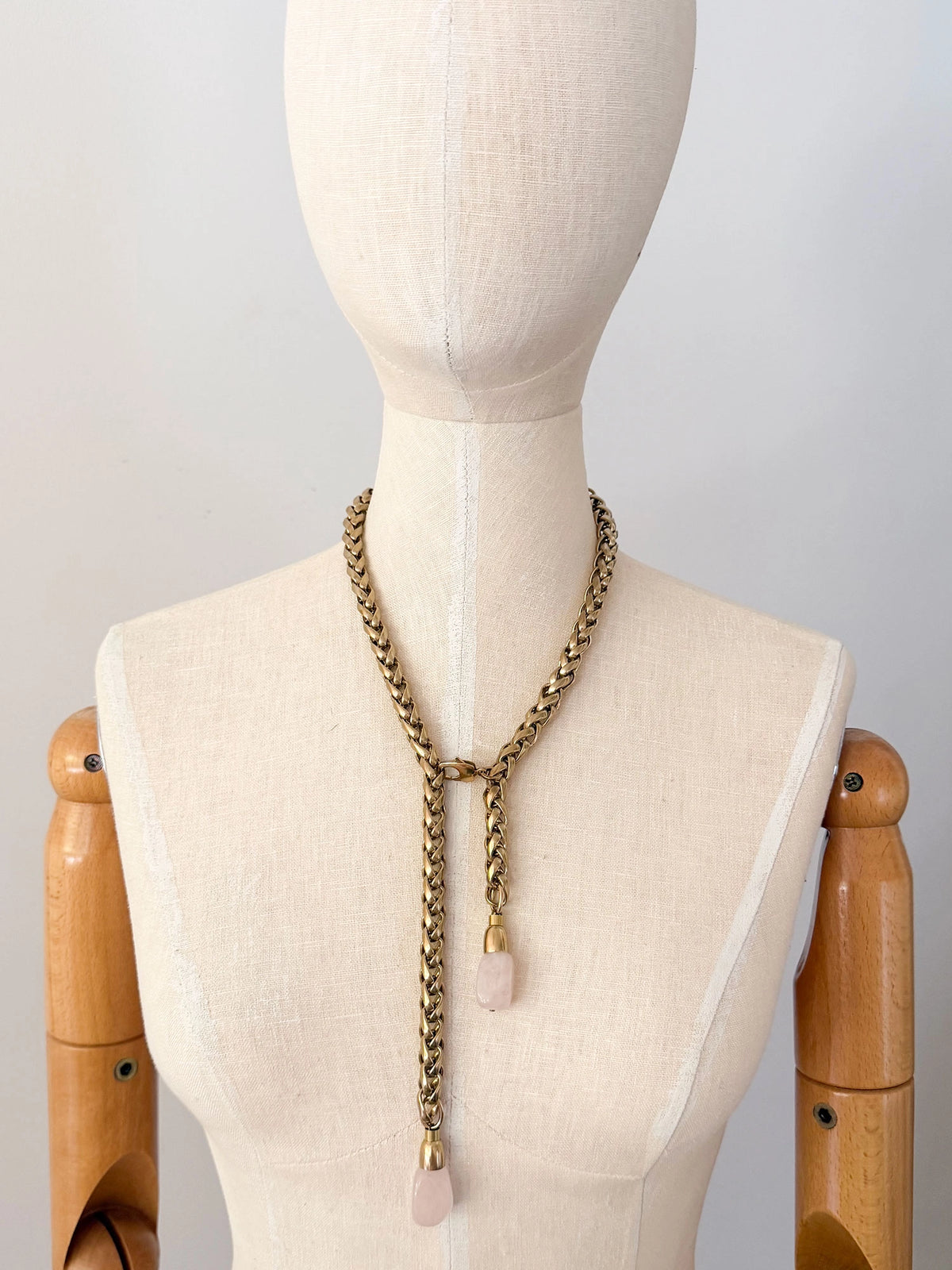 A brass chain lariat necklace knotted with two dangling light pink rose quartz teardrop-shaped beads at the bottom by Canadian jewelry designer Michelle Ross